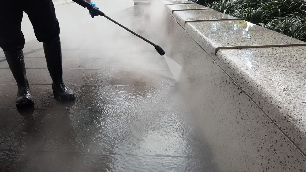 Person Pressure-washing A Wet Sidewalk Beside A Stone Curb — Port O' Call Cleaning In Cannon Valley, QLD