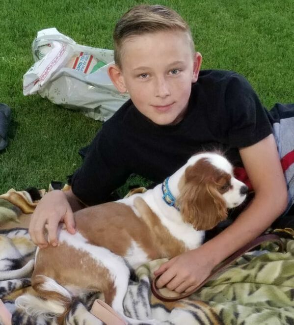 A boy is laying on a blanket with a brown and white dog