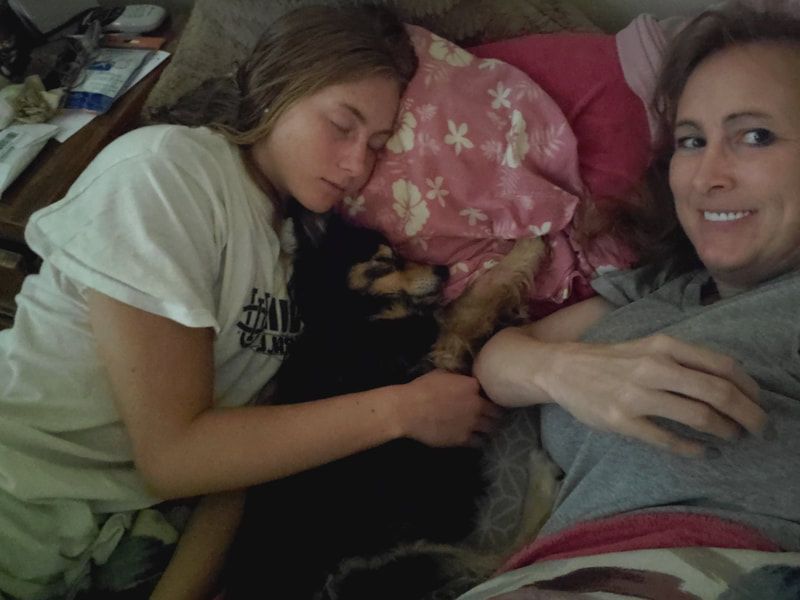 Two women laying on a bed with one wearing a shirt that says 