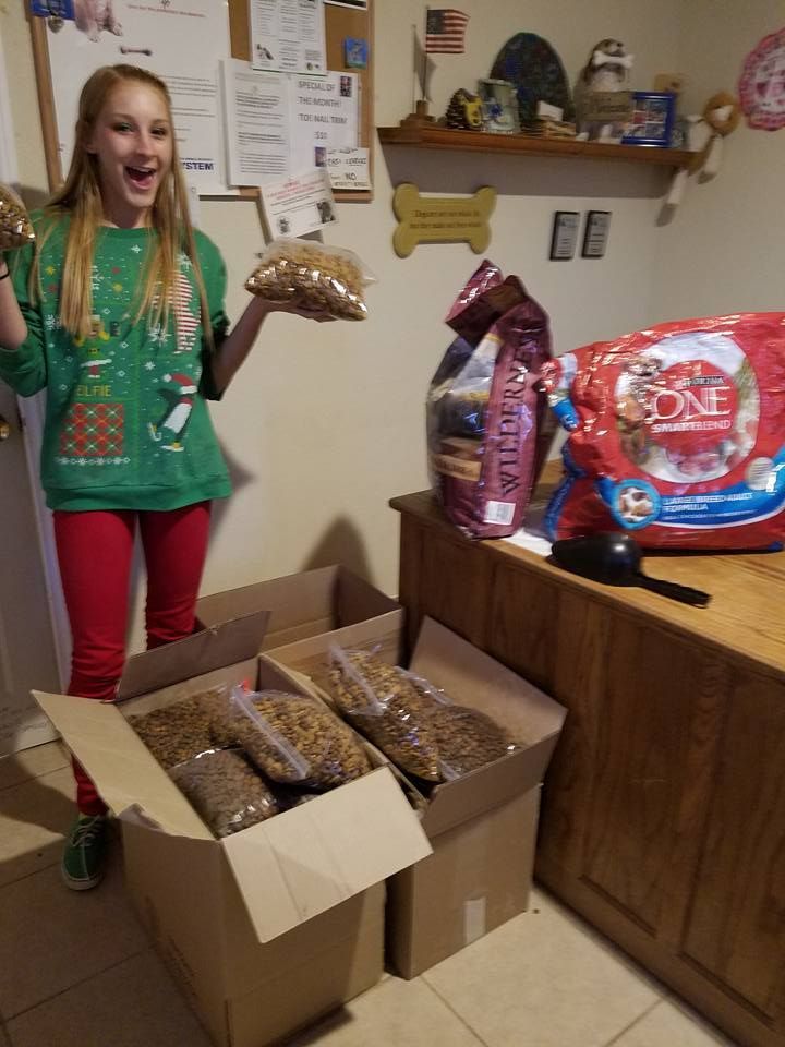 A girl in a christmas sweater is holding a bag of dog food