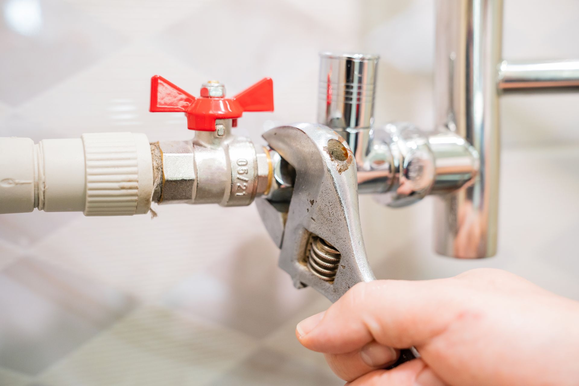 A person uses an adjustable wrench to tighten a metal valve fitting on a water pipe.