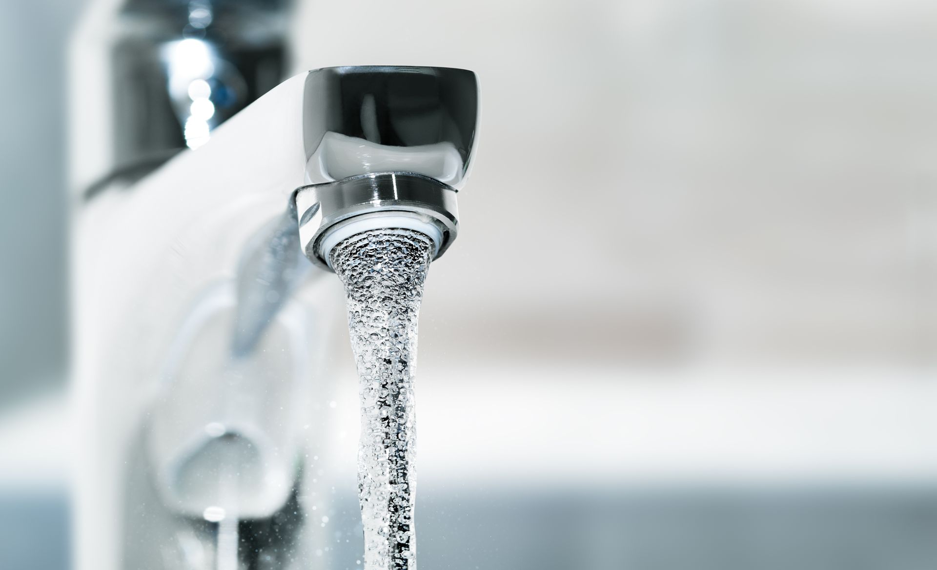 A modern chrome bathroom faucet with a white handle, running a steady stream of water into a sink.