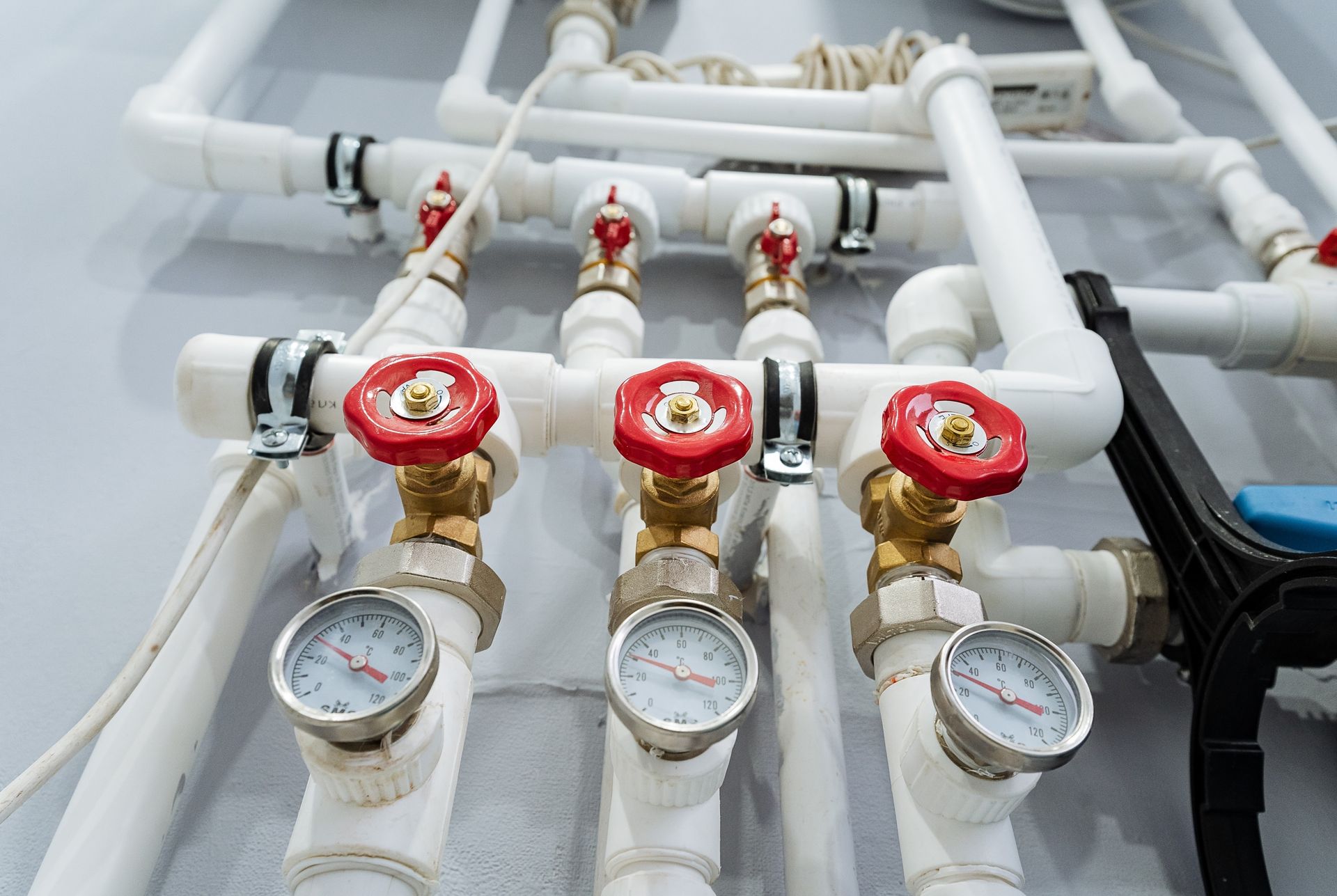 White pipes with three red-handled valves and pressure gauges attached to a wall.
