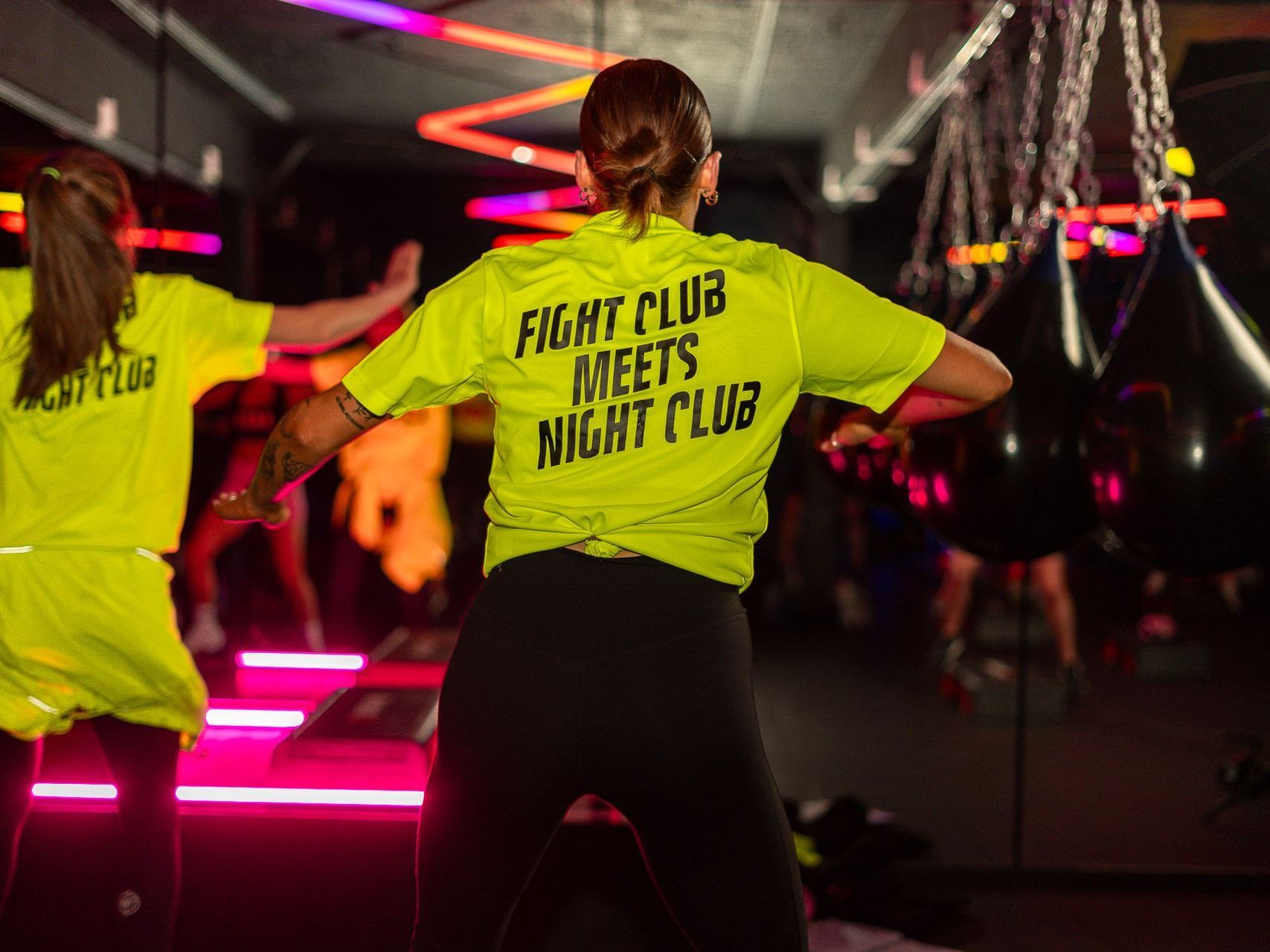 A woman in a neon yellow shirt is dancing in a gym.