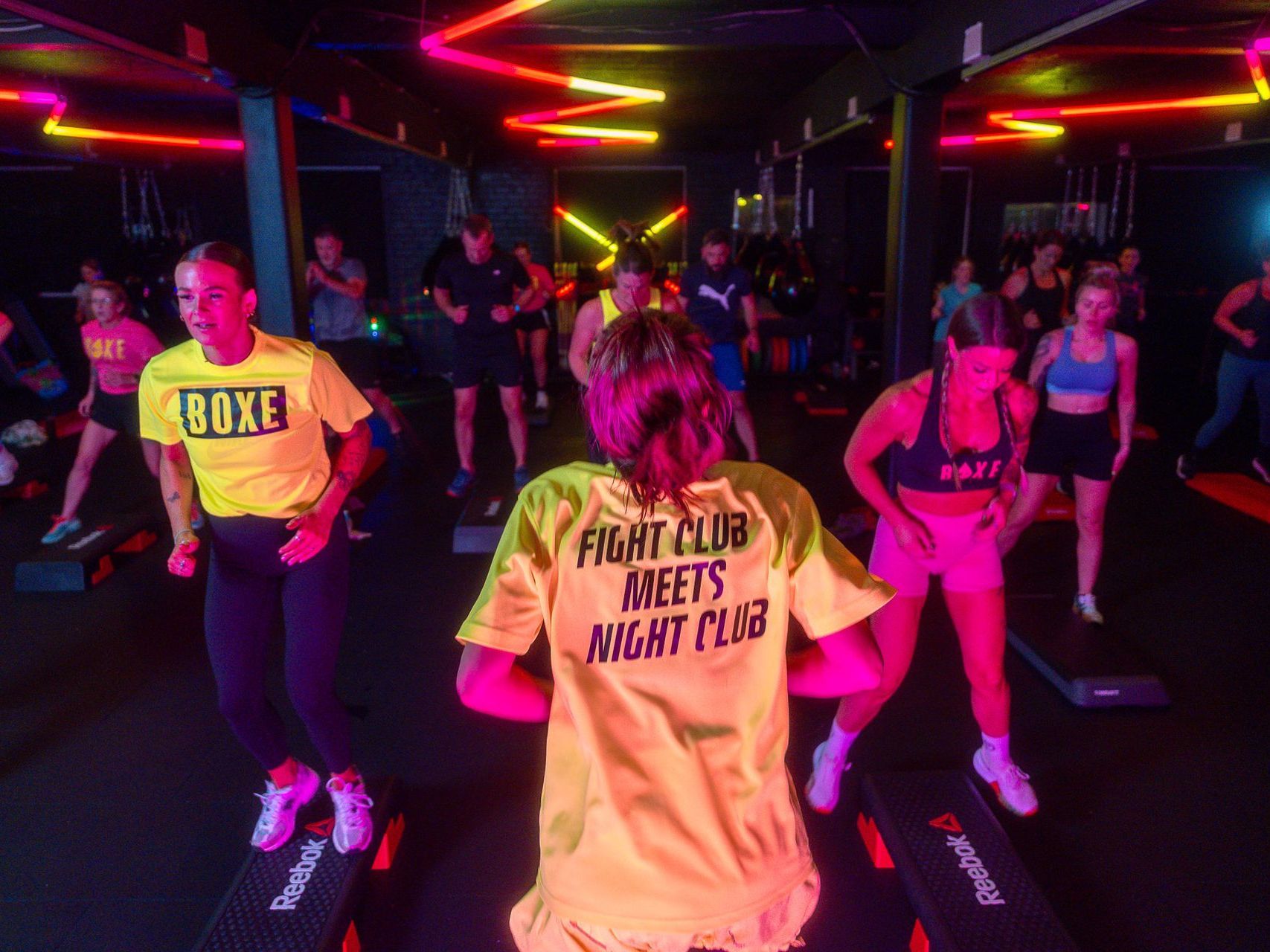 A group of people are dancing in a gym with neon lights.