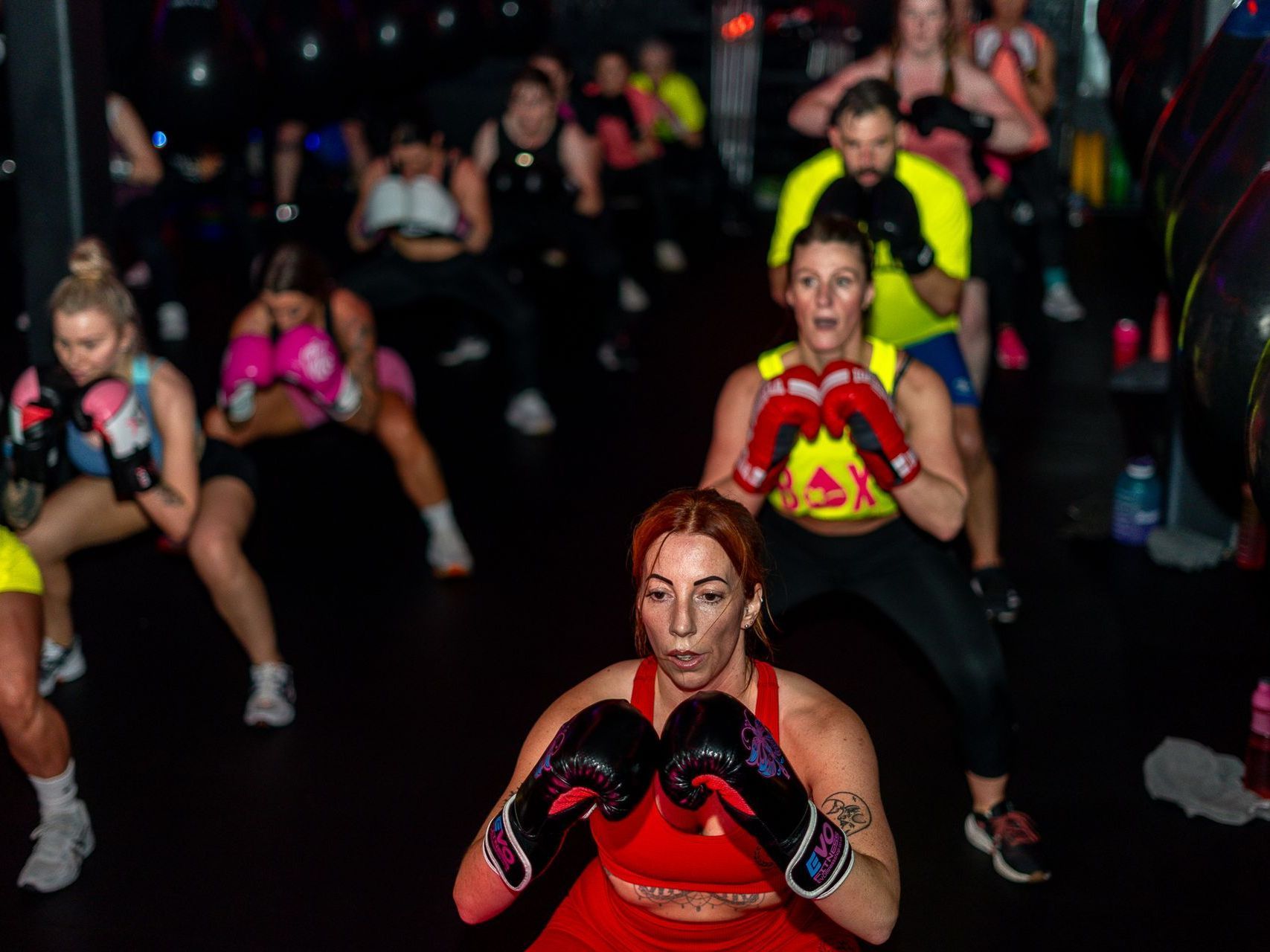 A group of people wearing boxing gloves are doing exercises in a gym.
