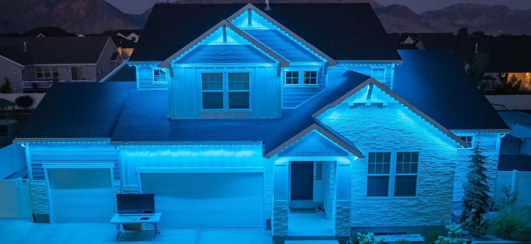 Blue-lit suburban house at night with snow on the roof and driveway, front exterior view