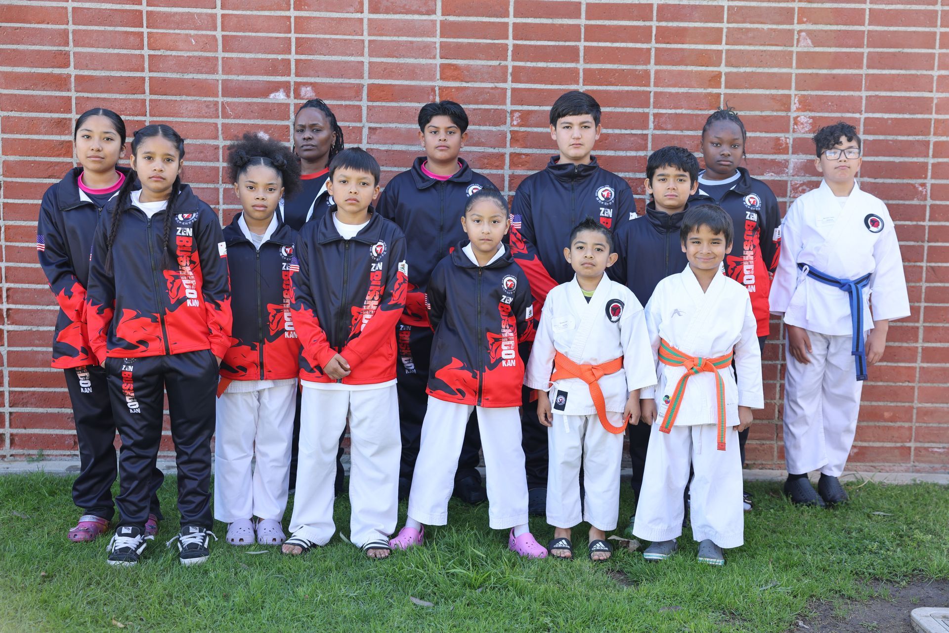 Group of children in martial arts uniforms posing in front of a brick wall.