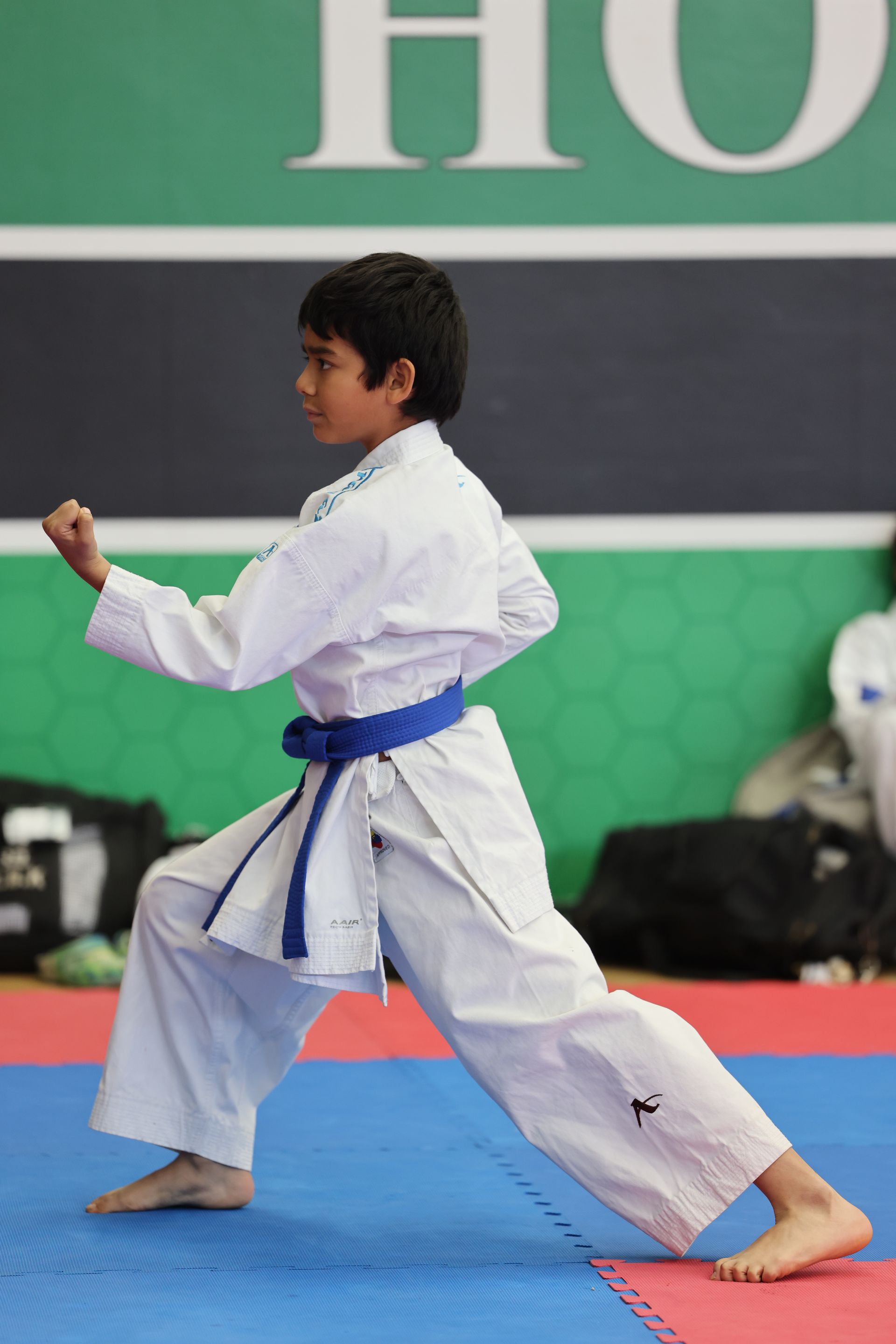 Boy in karate uniform, blue belt, in a fighting stance, on a blue and red mat.