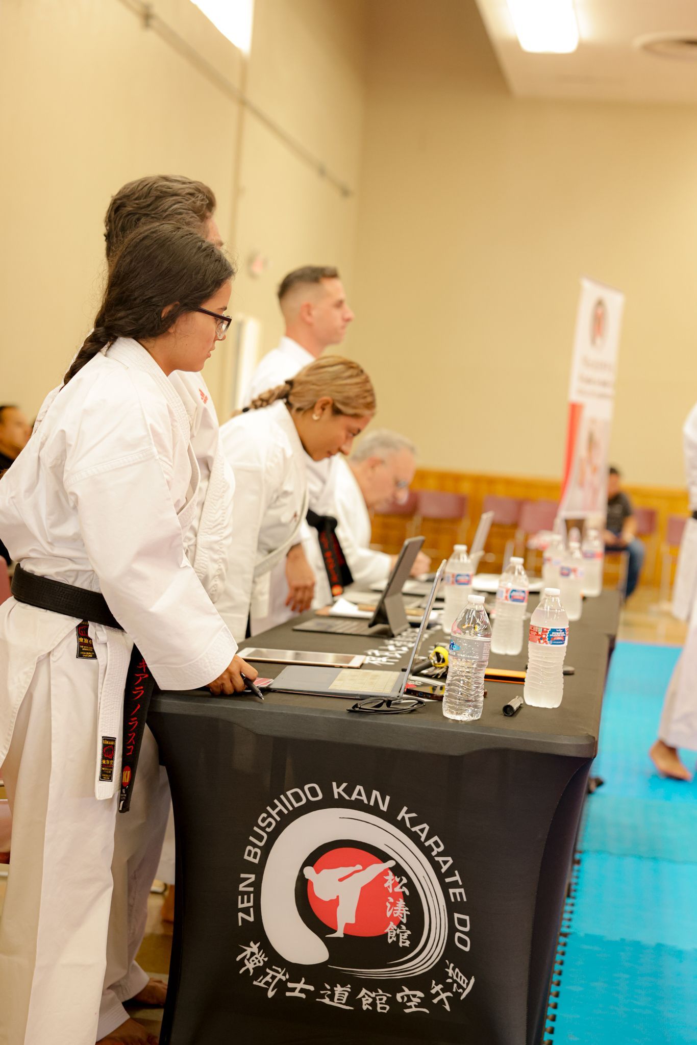 People at a judges table with a black banner  at an indoor event.