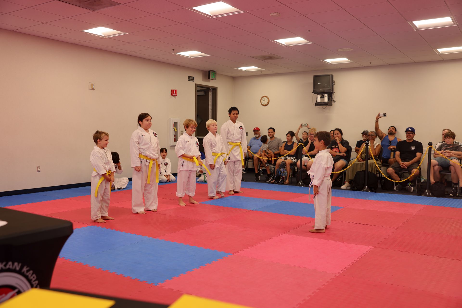 Martial arts class with students in white uniforms standing on red and blue mats in a gymnasium