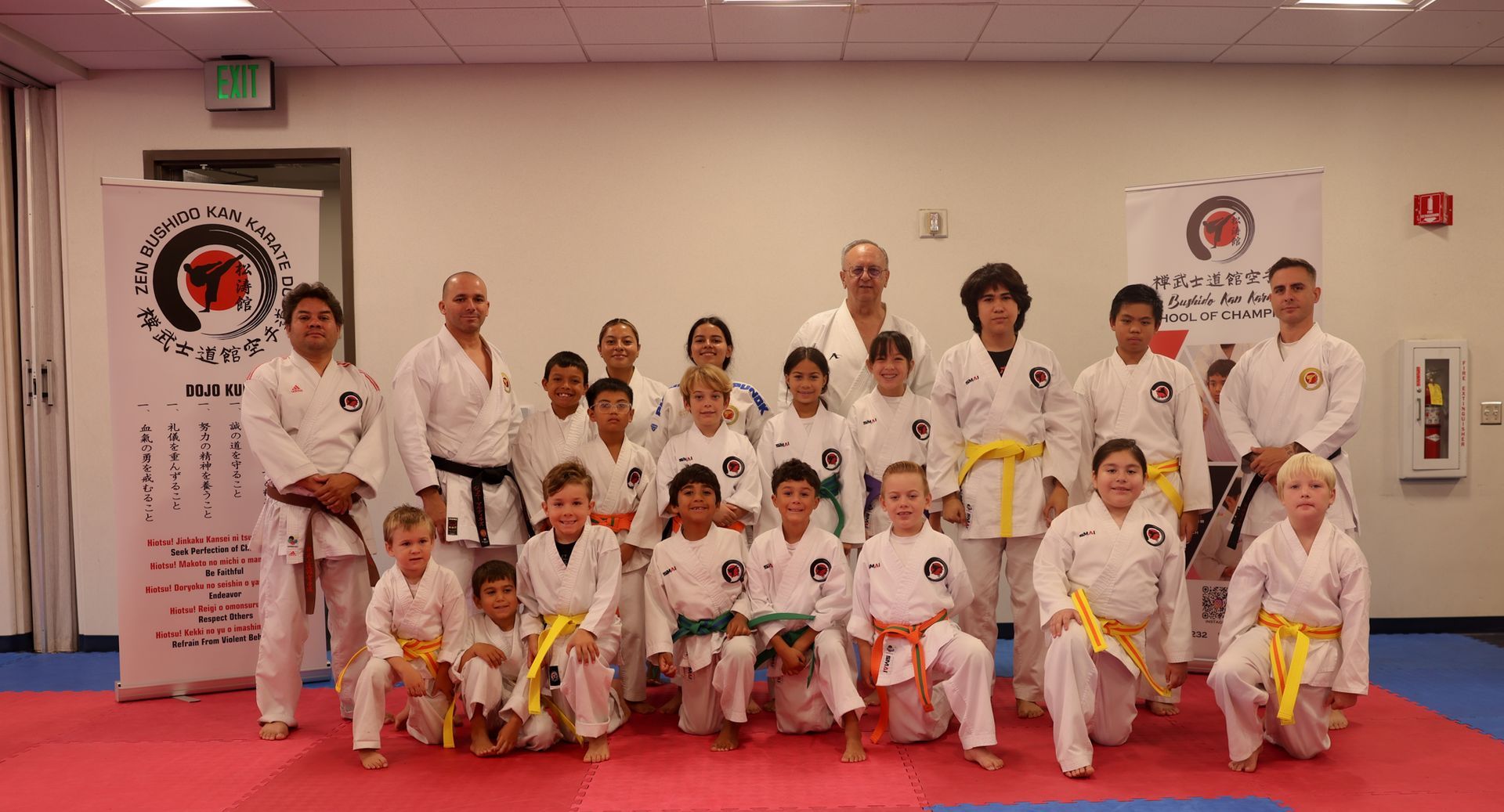 Martial arts class group posing in white uniforms and belts on red mats inside a dojo