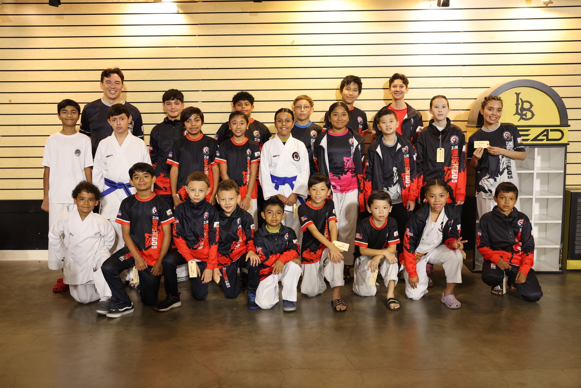 Group of people posing indoors in matching black, red, and white sports uniforms on a wood floor