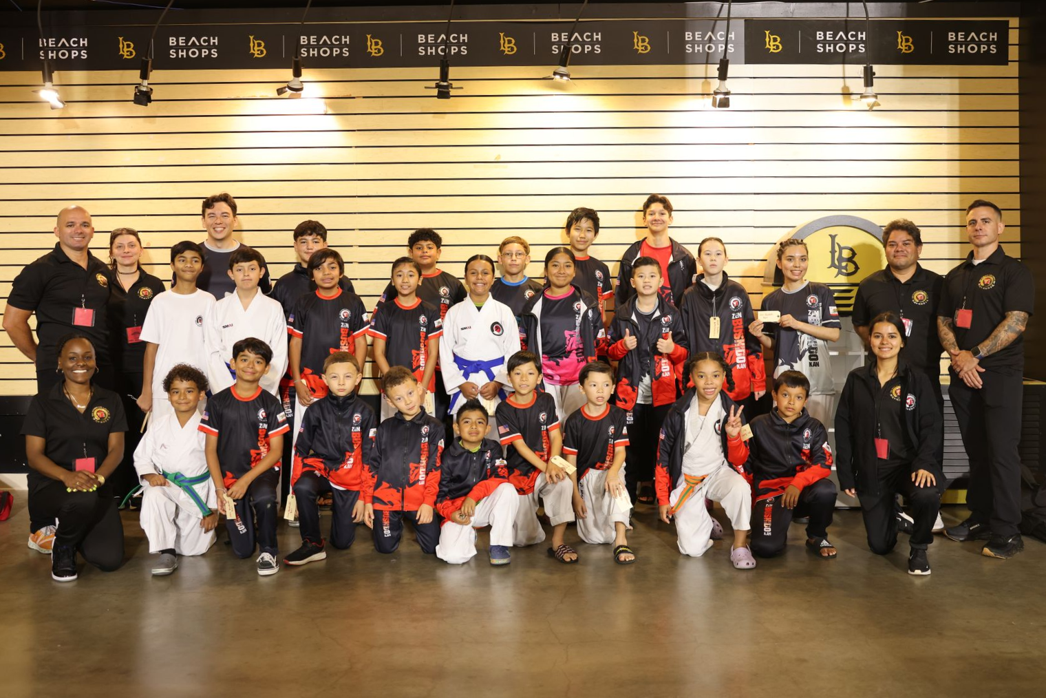Group of people posing for a team photo indoors, many in black and red uniforms, standing and kneeling together.