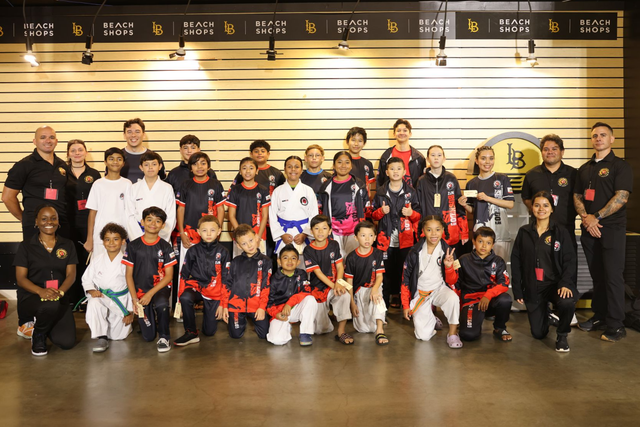 Group of people posing for a team photo indoors, many in black and red uniforms, standing and kneeling together.