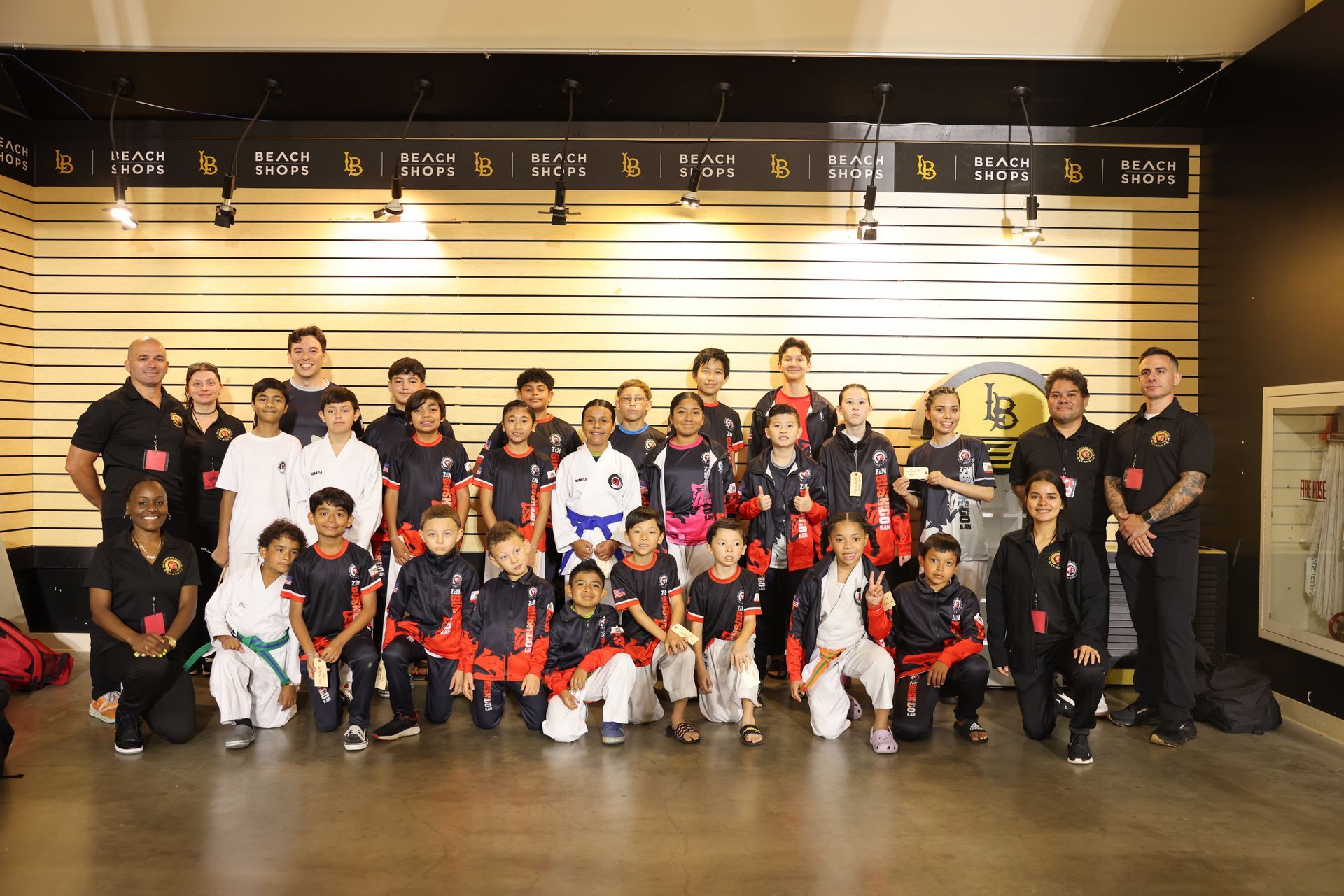 Large group posing for a team photo in a lobby, with children in red, black, and white uniforms.