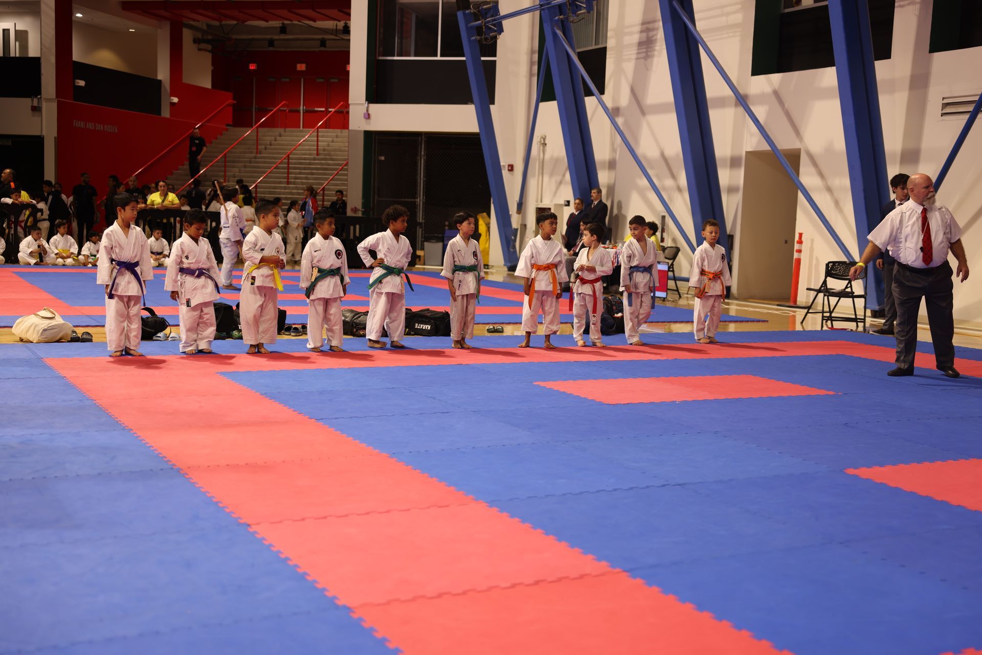 Karate class practicing on red and blue mats in a gymnasium