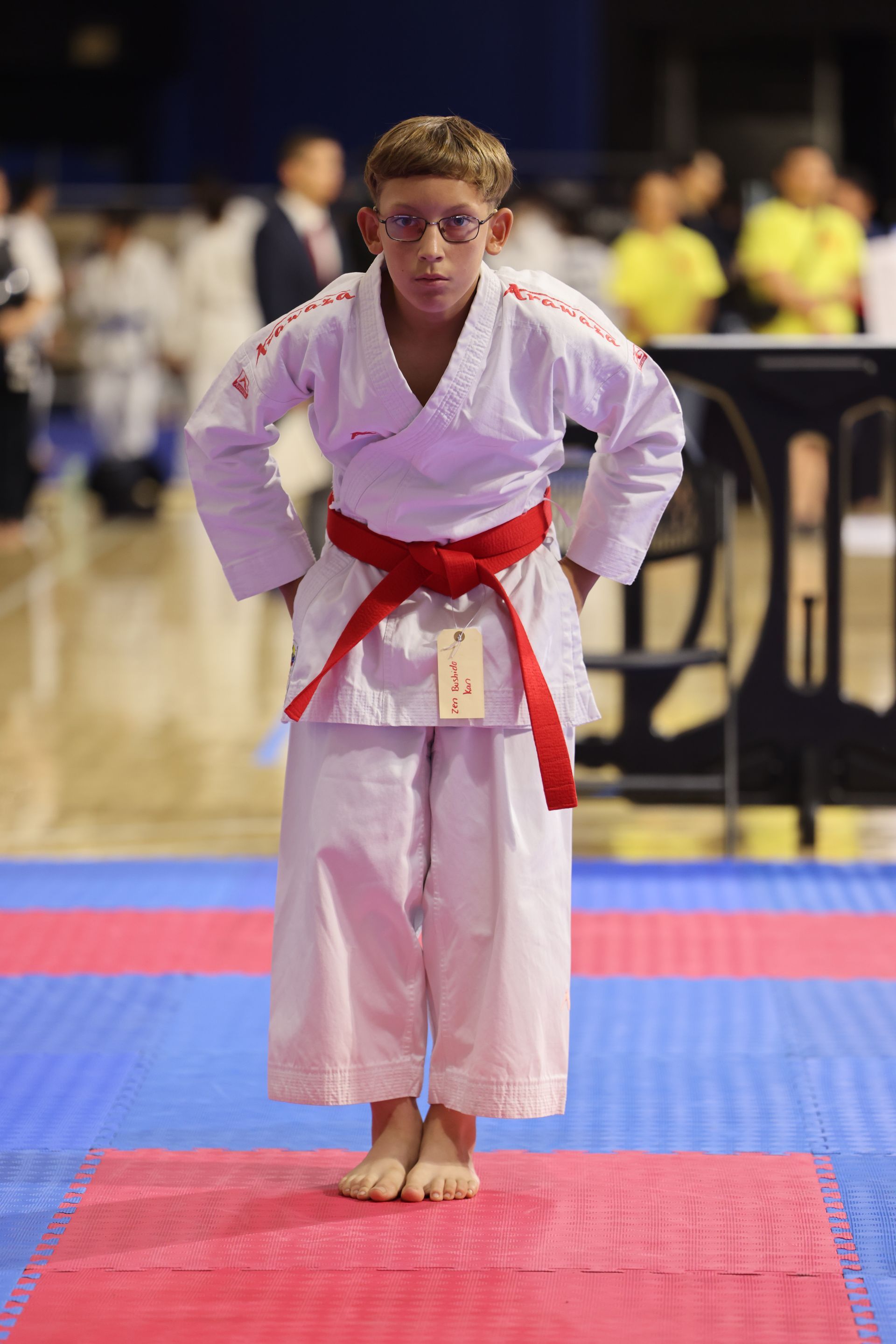 Karate competitor in white gi and red belt bows on a tatami mat at a tournament.
