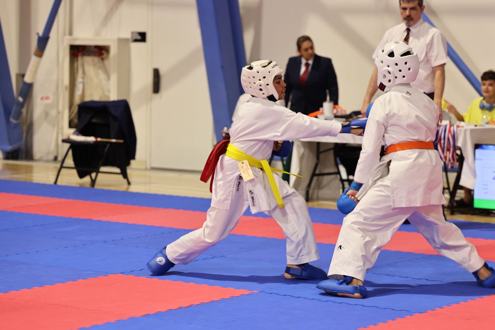 Two helmeted fencers in white spar on a blue-and-red competition mat