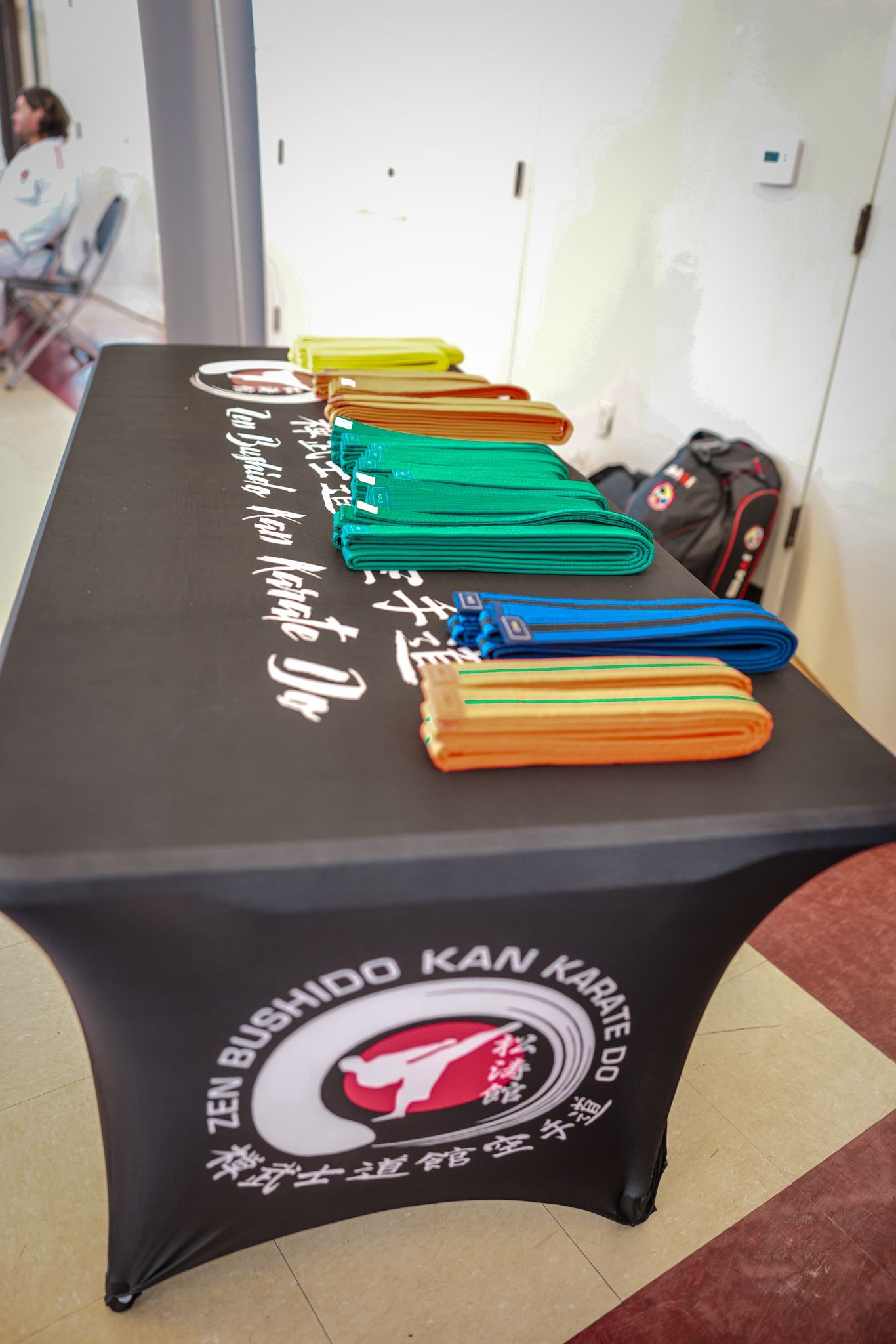 Folded karate belts in yellow, orange, green, and blue are arranged on a black table with a 