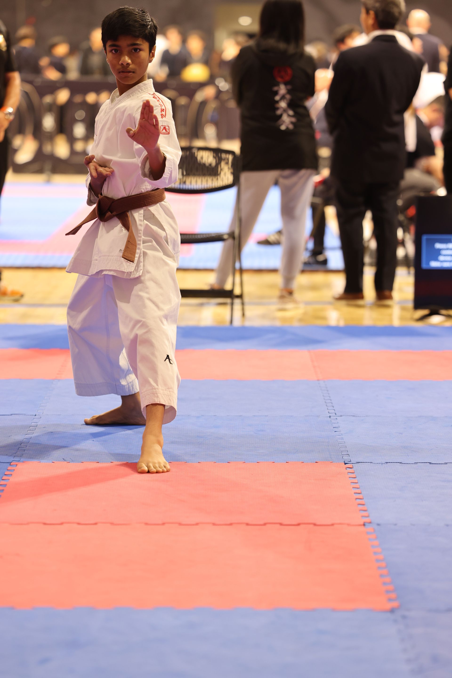 Martial arts competitor in white gi posing on a red and blue mat at an indoor event
