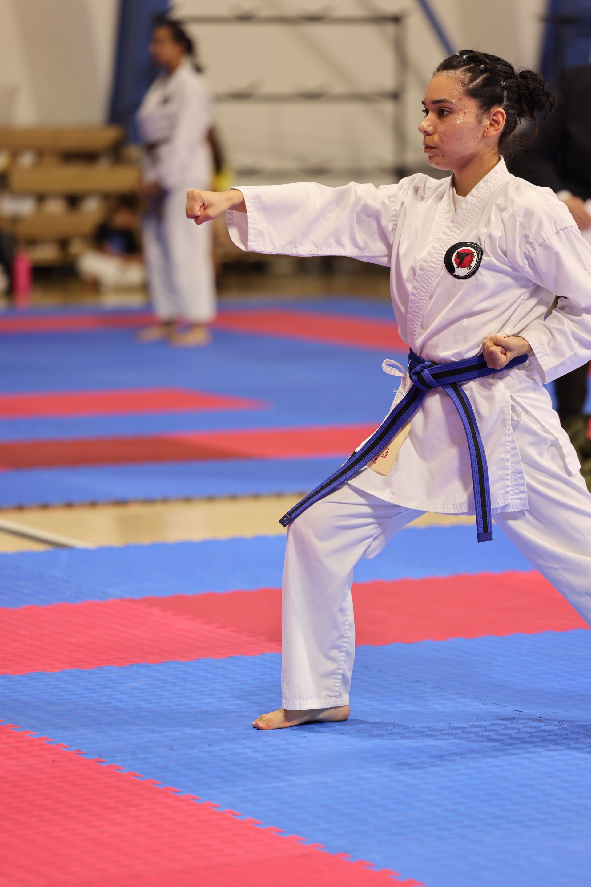 Martial artist in white gi with blue belt performing a punch on a competition mat