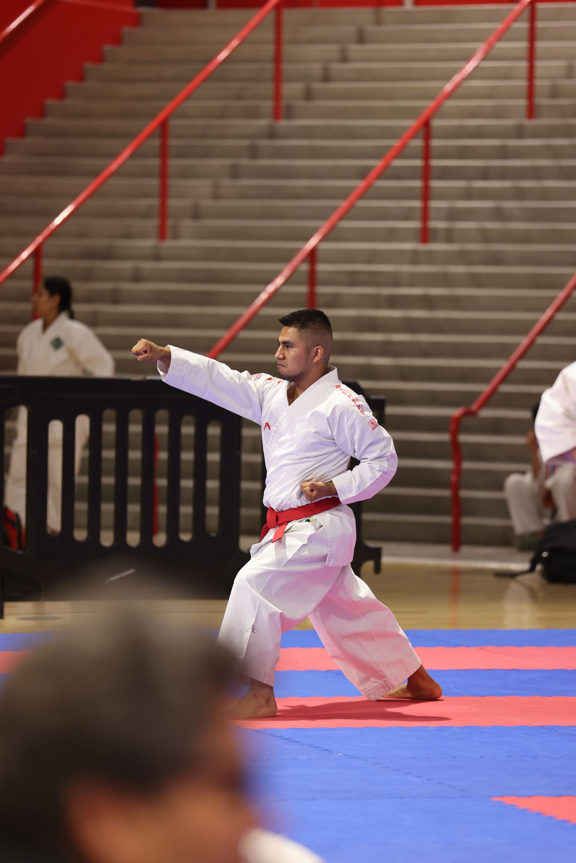 Martial artist in white gi performing a kata on blue and red mats in a gymnasium