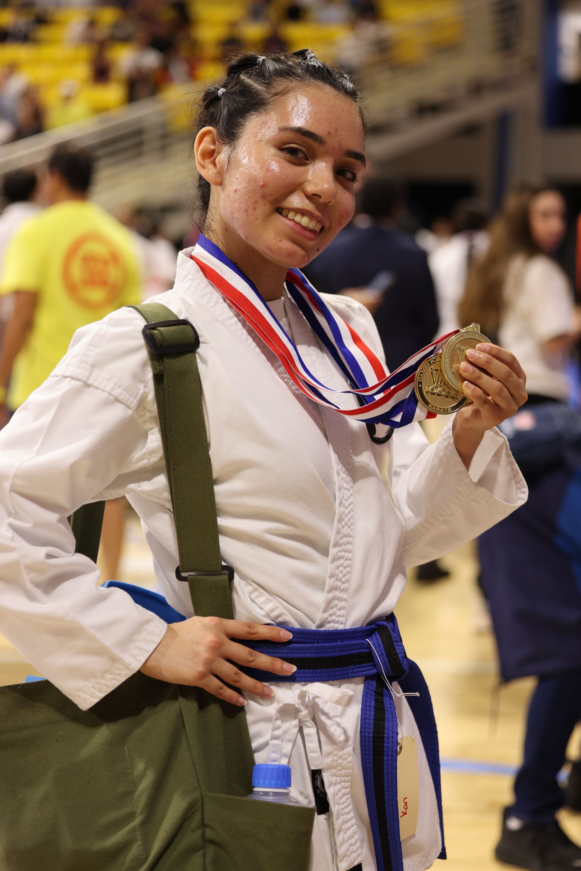 Athlete in white gi with blue belt smiling and holding a medal in a gymnasium