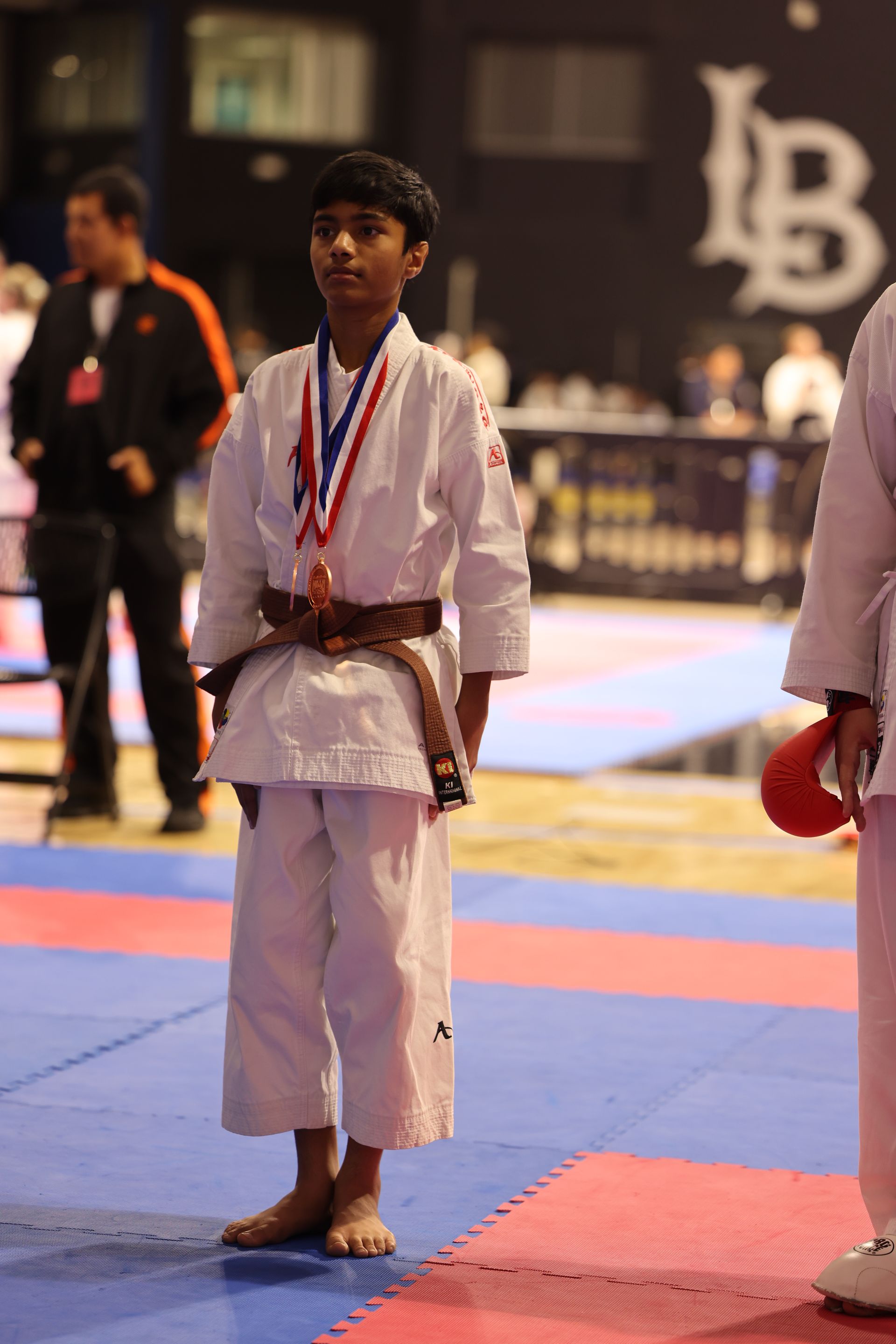 Martial arts competitor in white gi with medals standing on a mat at an indoor event