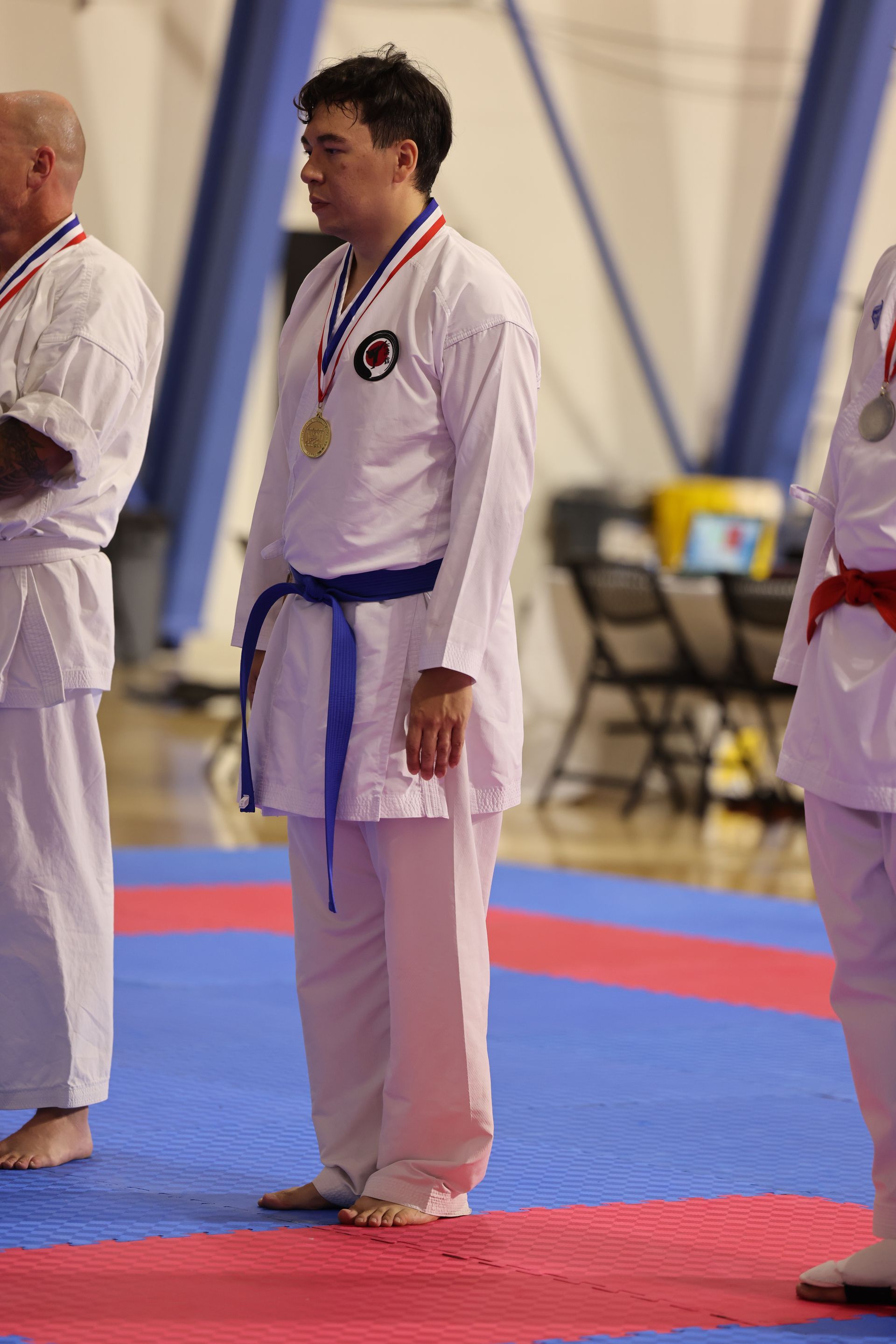Martial arts competitor in white uniform and medal standing on blue and red mats indoors