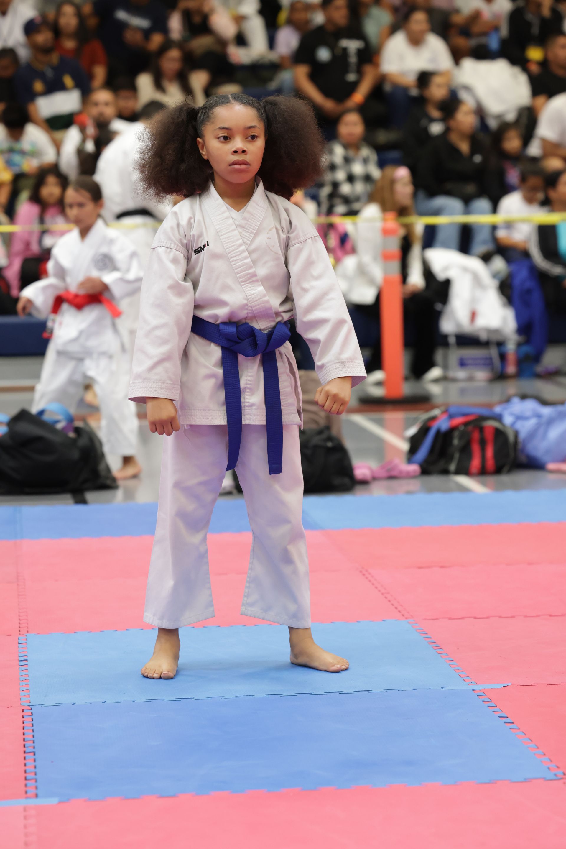 Young martial artist in white gi with purple belt standing on blue mat at a competition