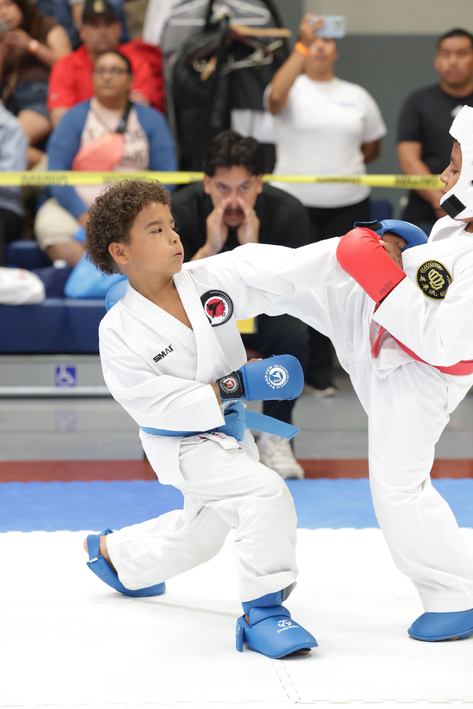 Two martial artists in white gis sparring on a mat, with one landing a kick in a competition setting