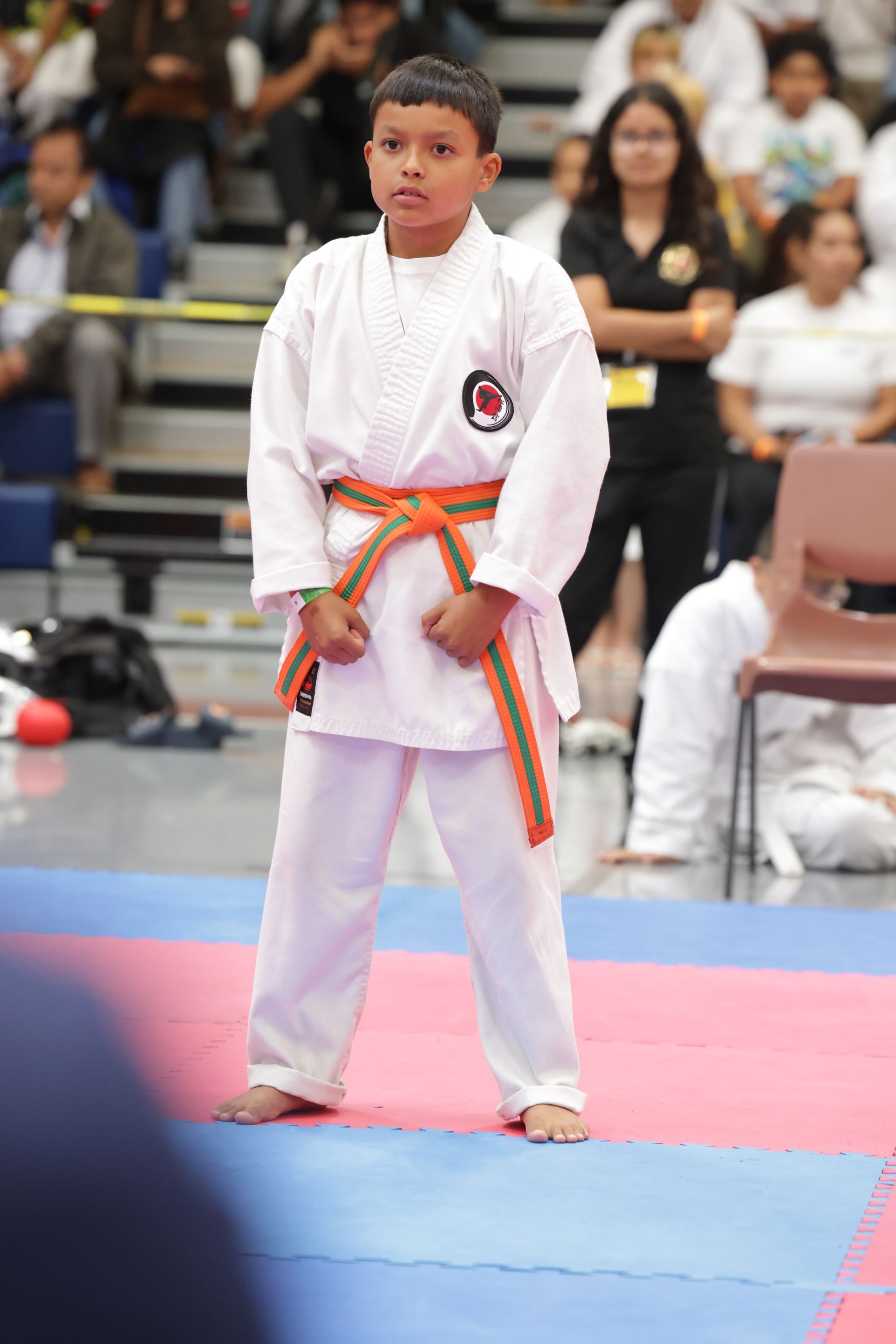 Young martial artist in a white gi with a striped belt standing on a mat during a competition