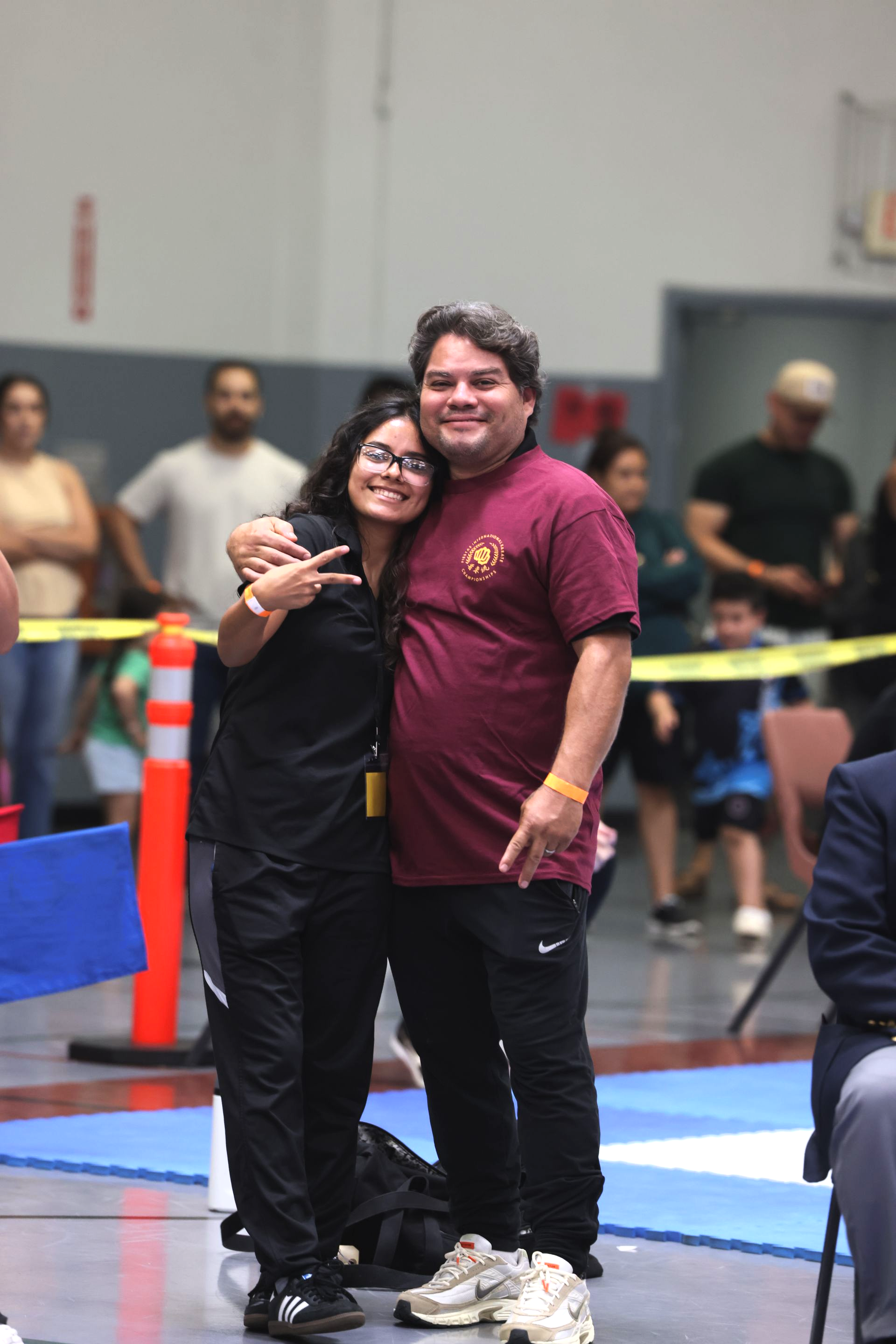 Two people smiling and hugging on an indoor sports court with spectators in the background