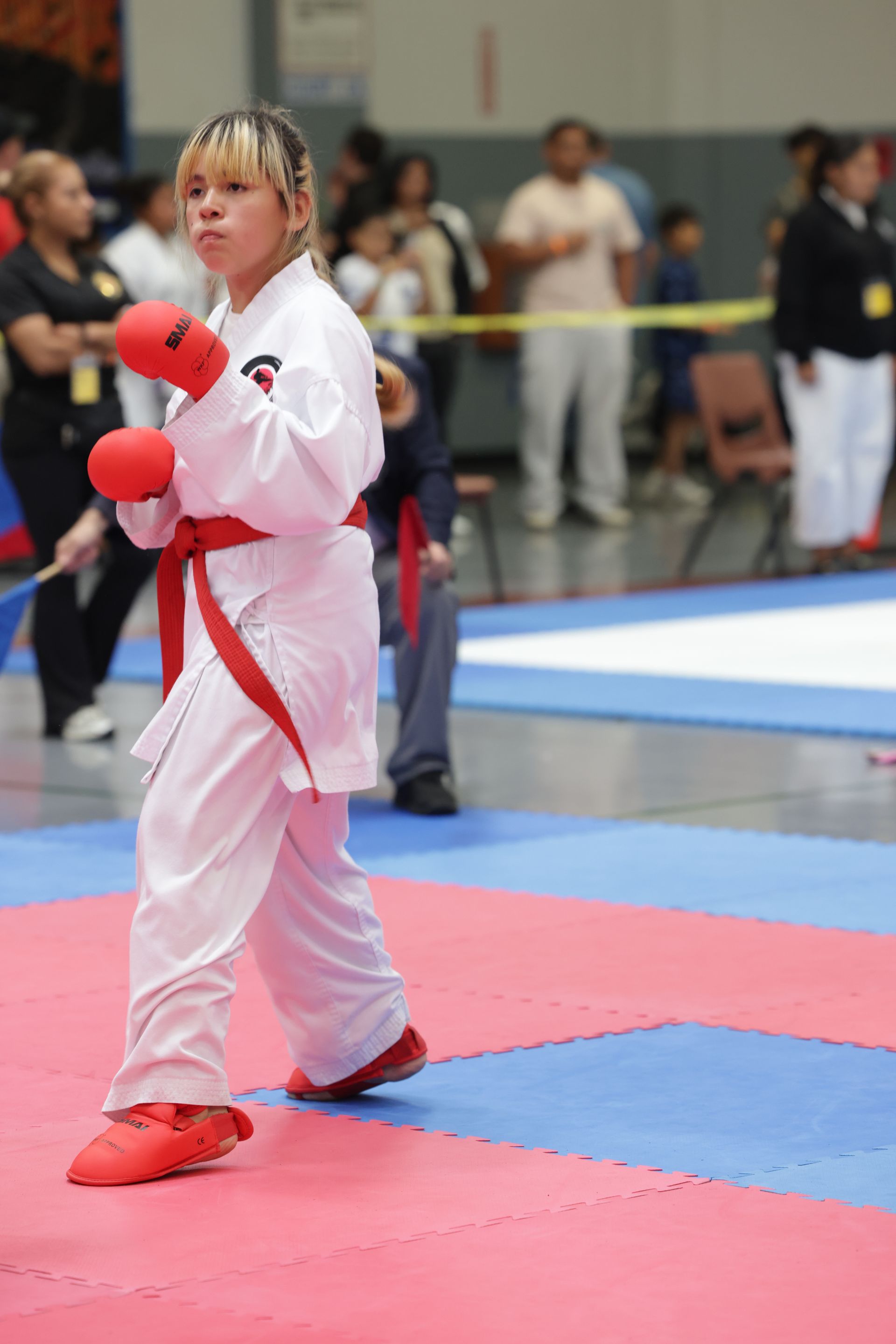 Karate competitor in white gi and red gloves stands on a mat during a martial arts match