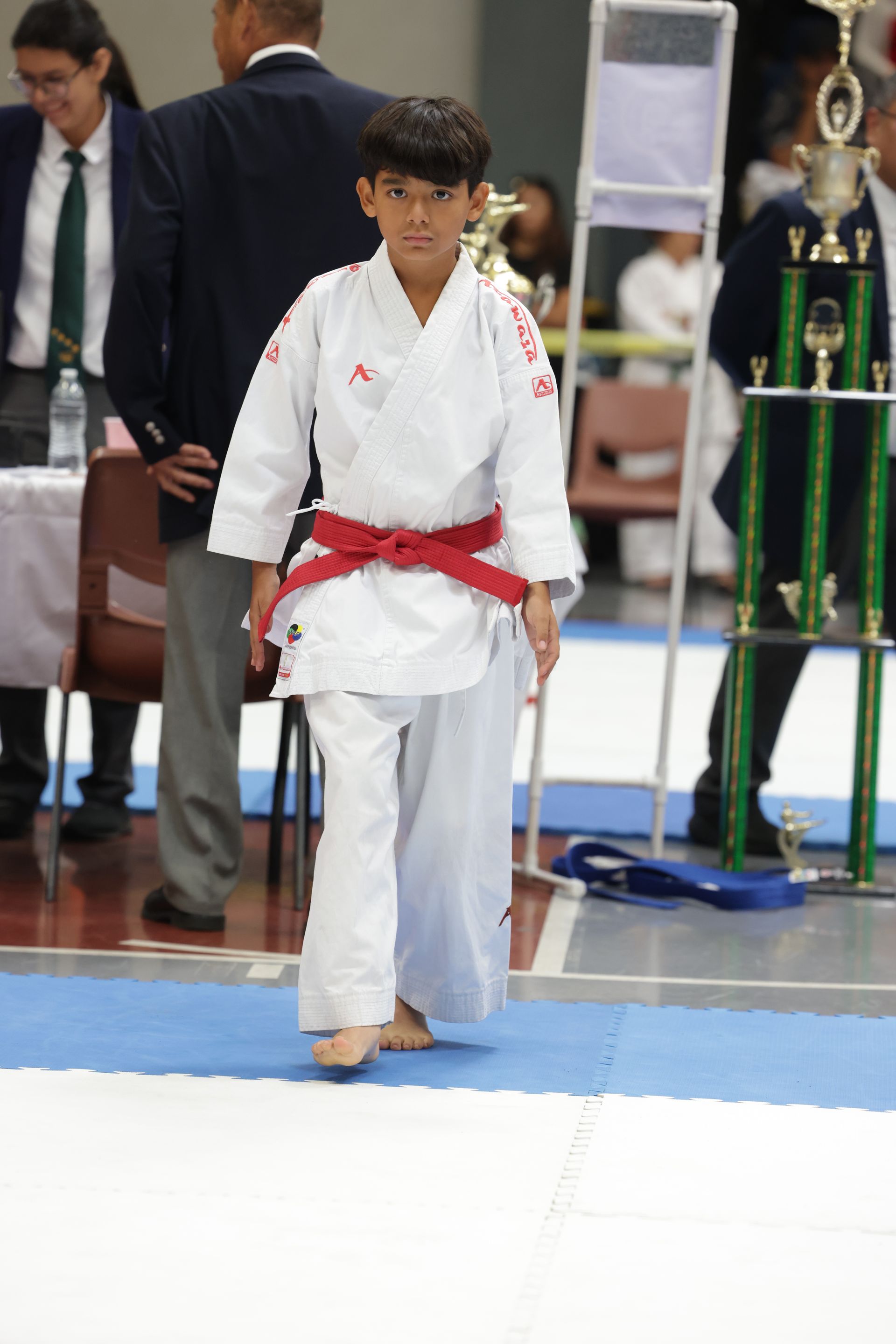 Karate competitor in white gi and red belt stands on a mat during a tournament
