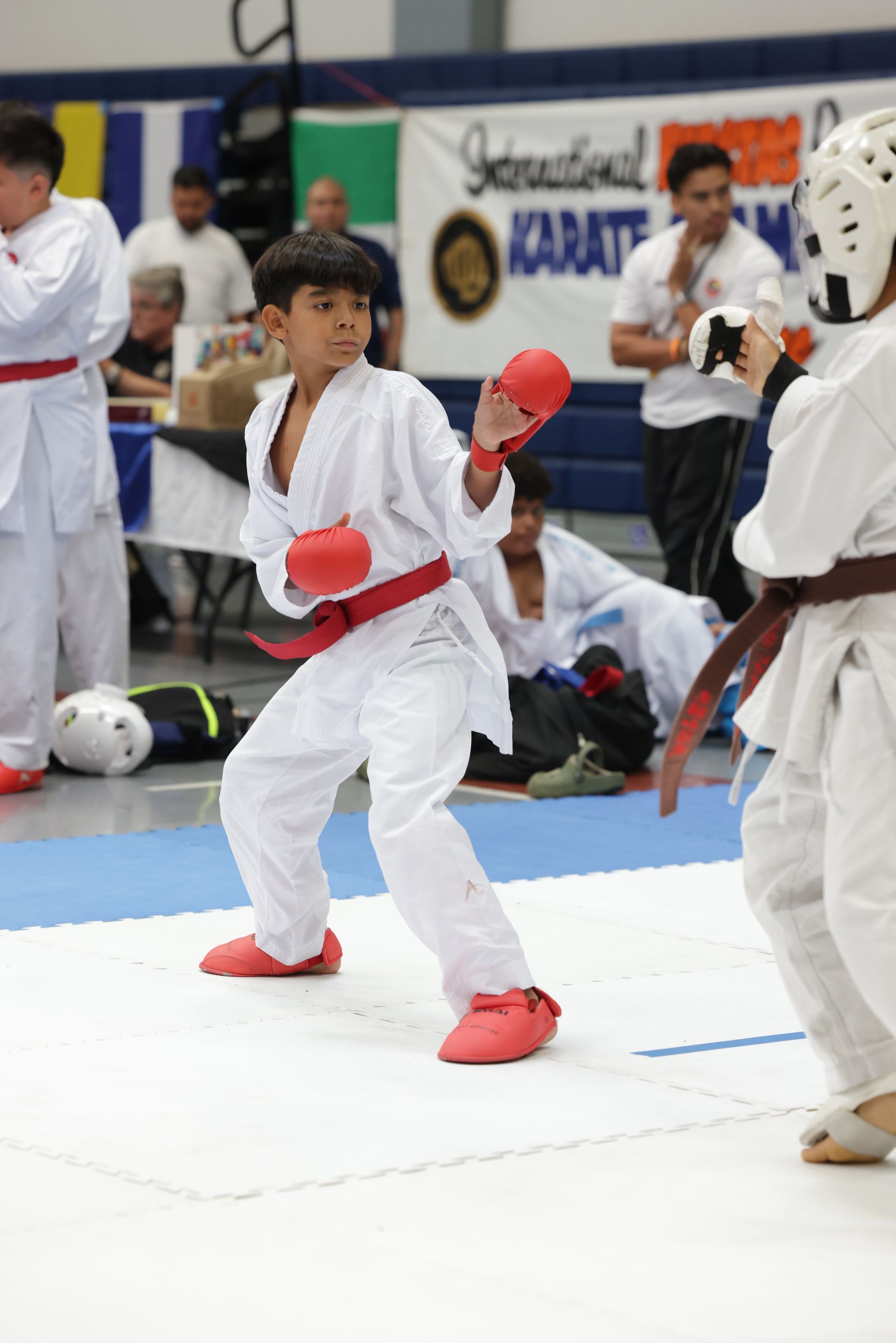Karate sparring match with two children in white uniforms and red protective gear on a competition mat
