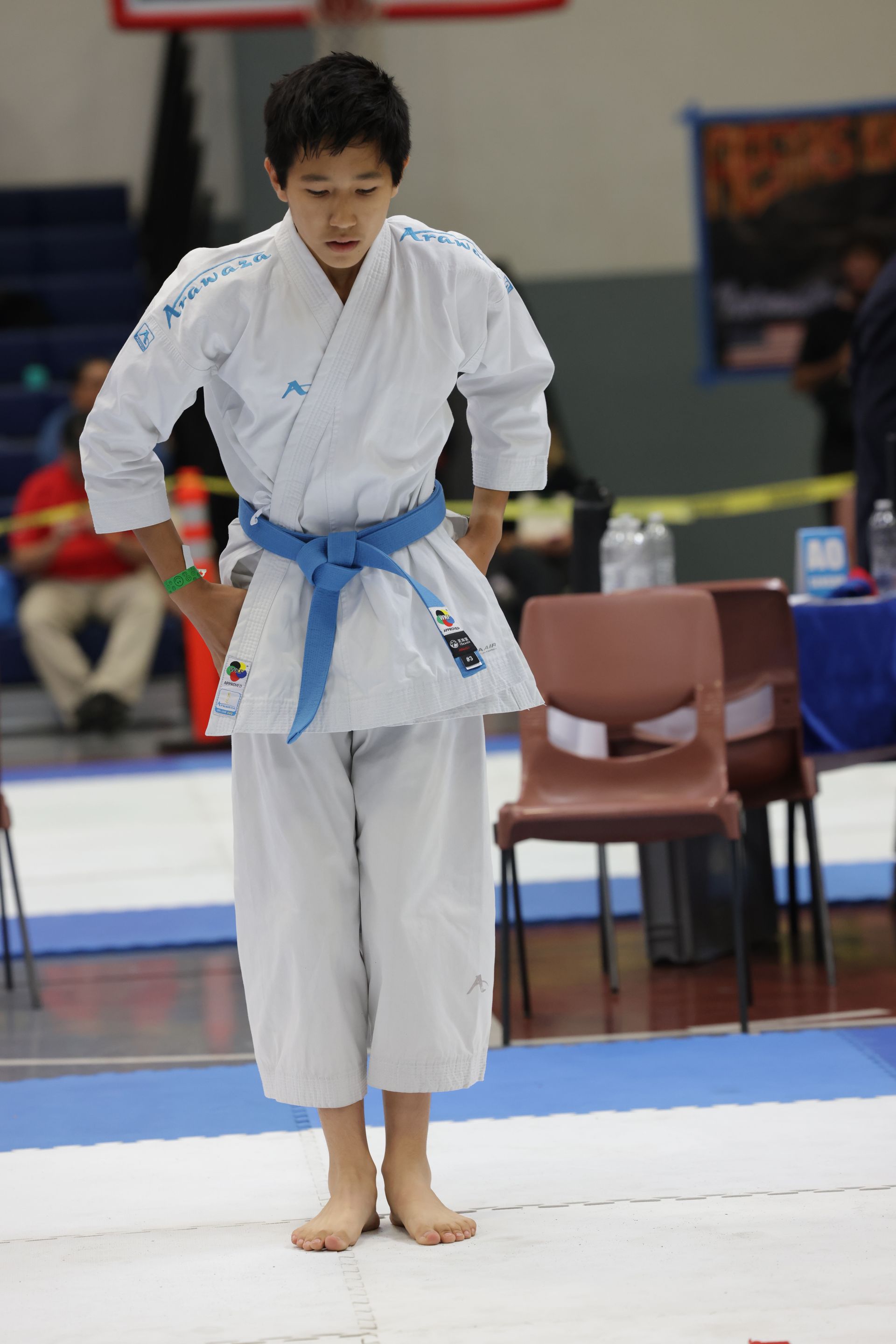 Martial artist in a white gi with blue belt standing barefoot on a competition mat