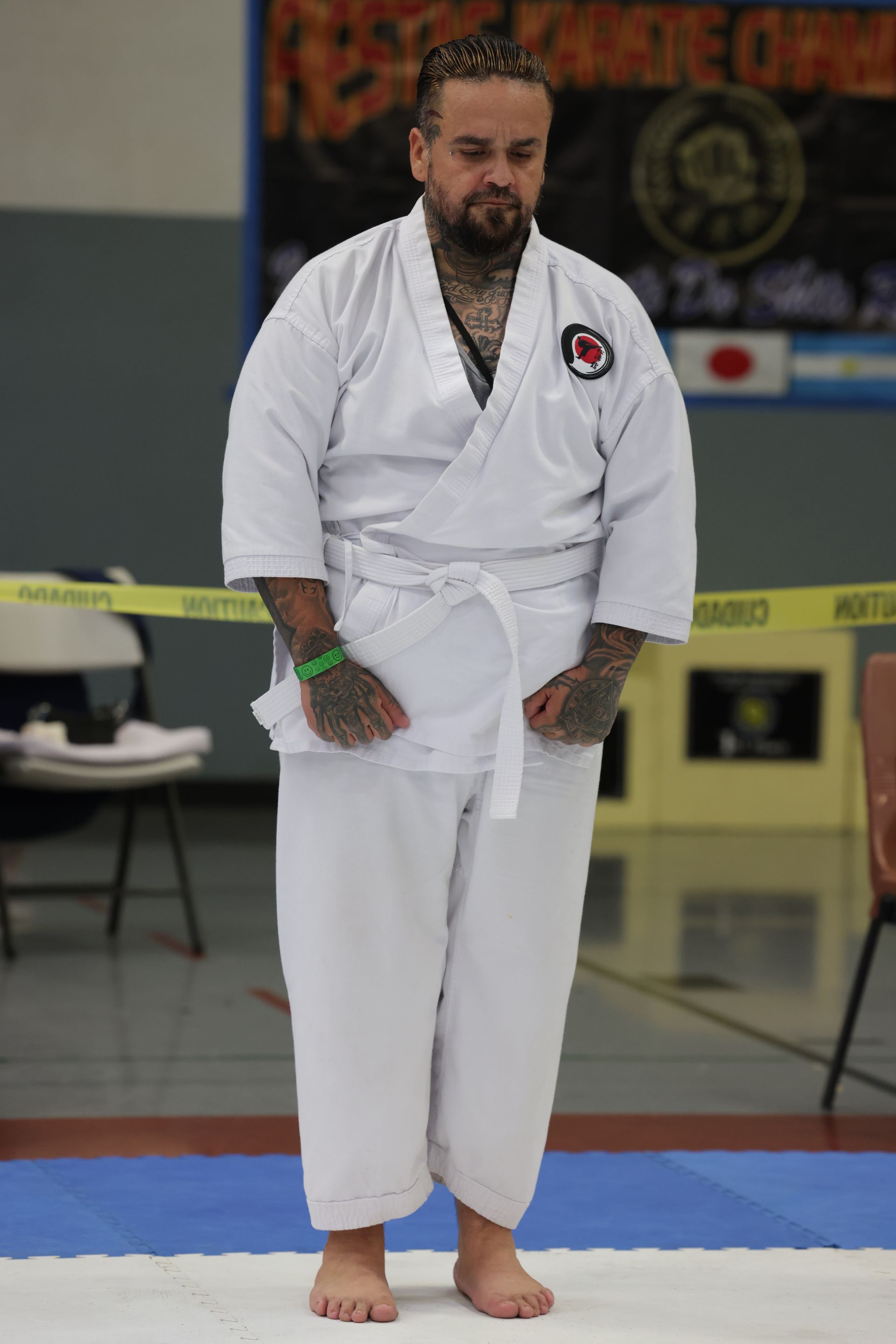 Man in a white gi stands barefoot on a mat at an indoor martial arts event.