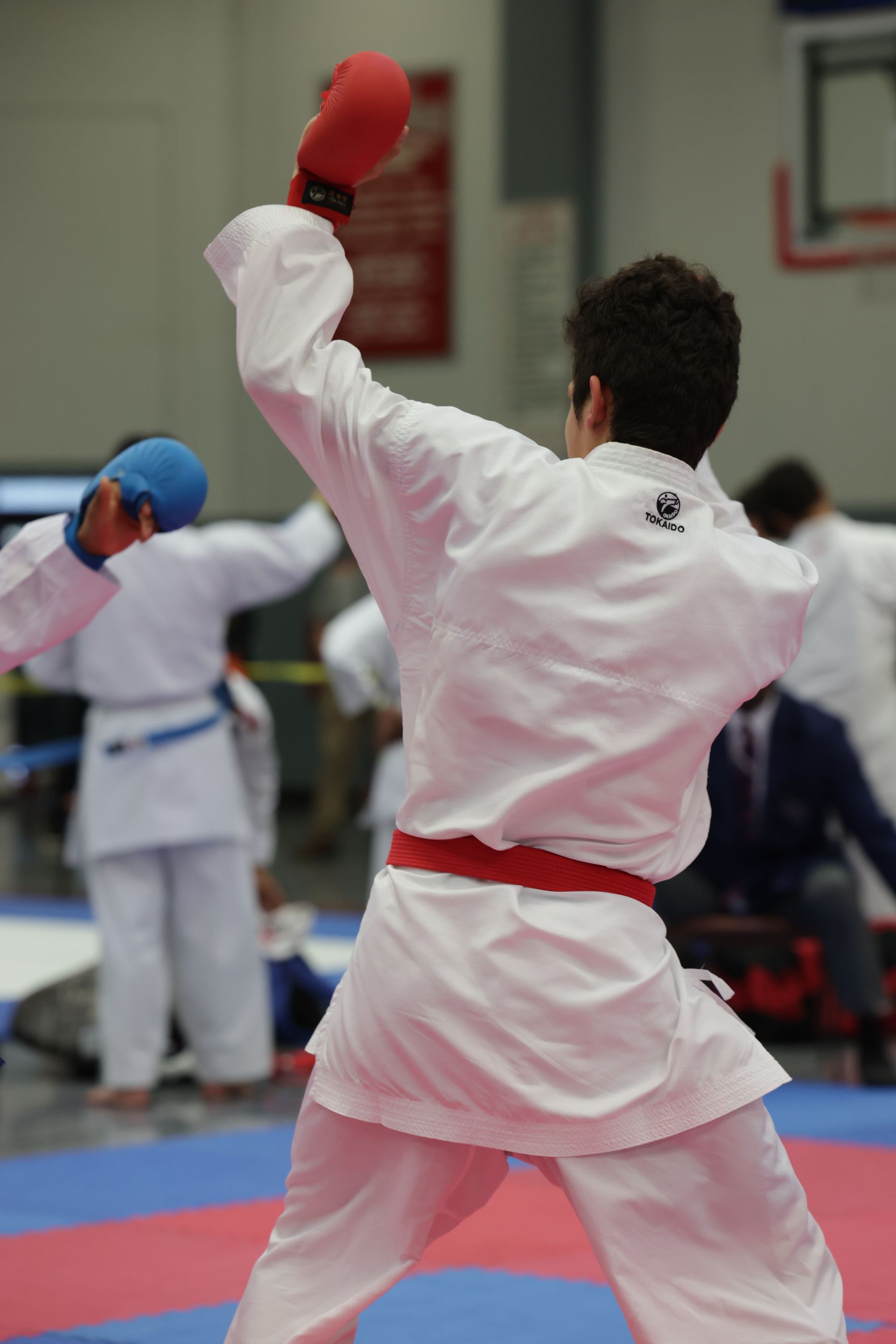 Karate competitors in white uniforms sparring on a mat, one raising a red-gloved arm