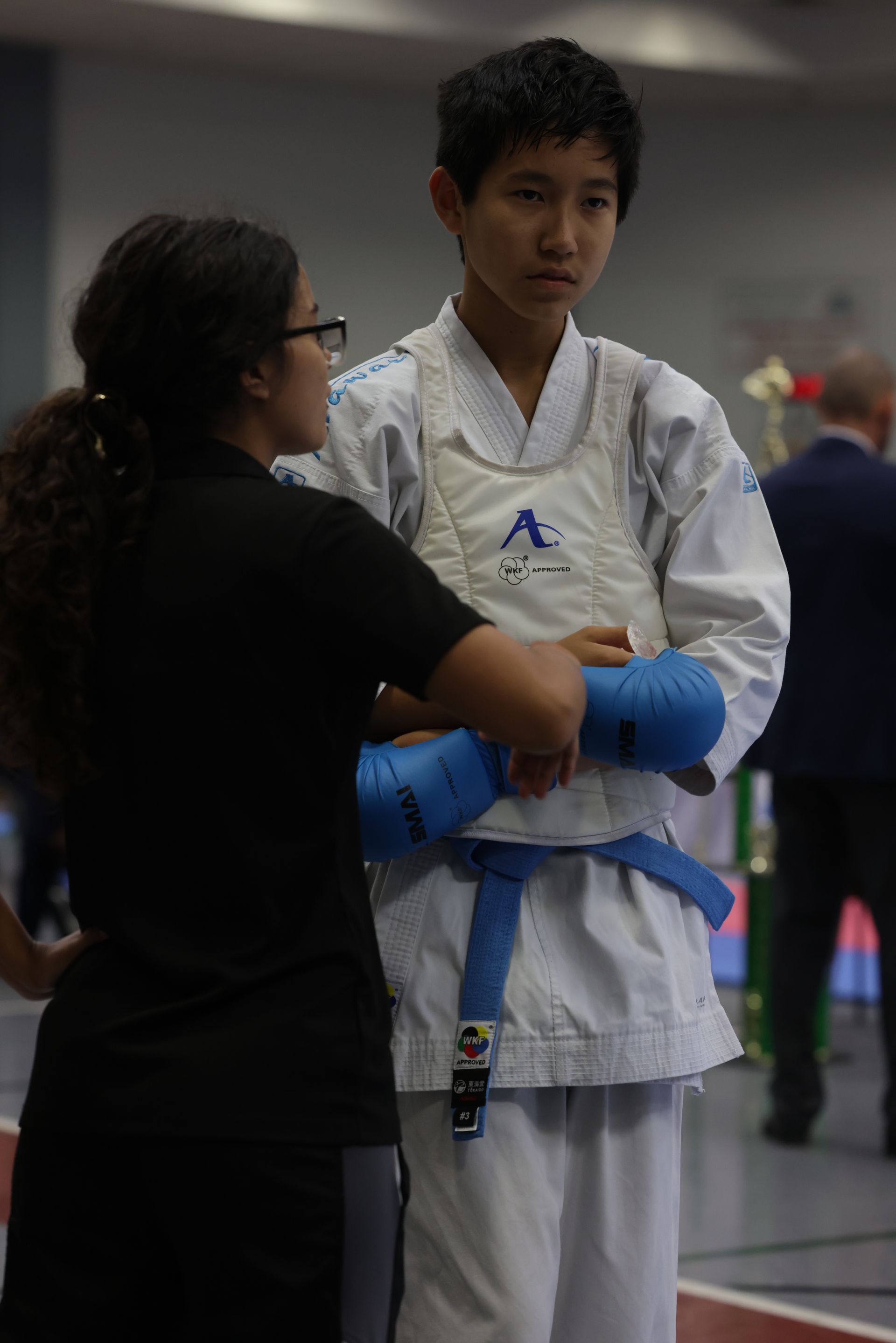 Martial arts instructor adjusting a student’s blue gloves during training in a gym