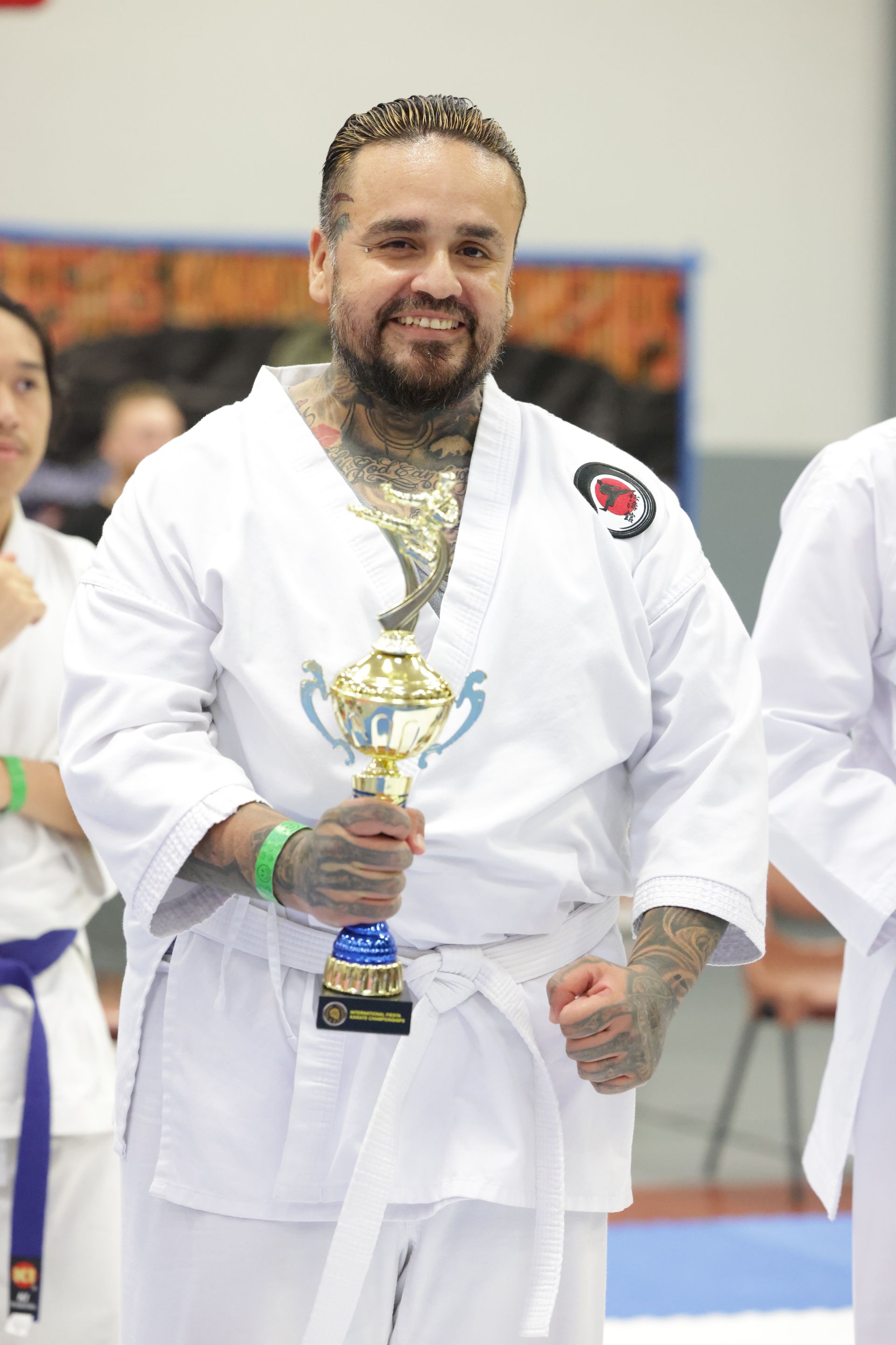 Martial artist in white gi holding a trophy at an indoor ceremony