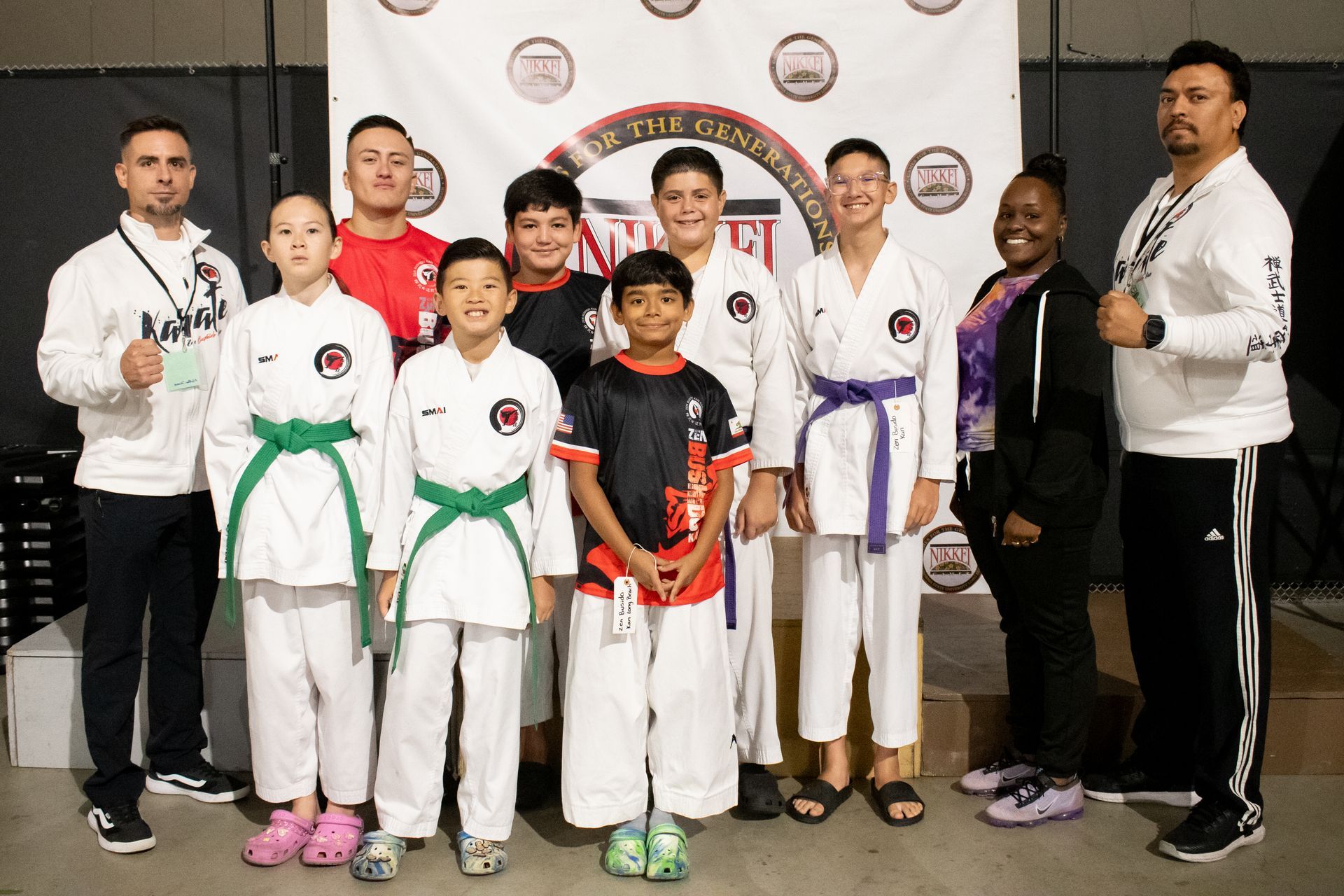 Group of karate students, instructors, and supporters posing in front of a banner at an event.