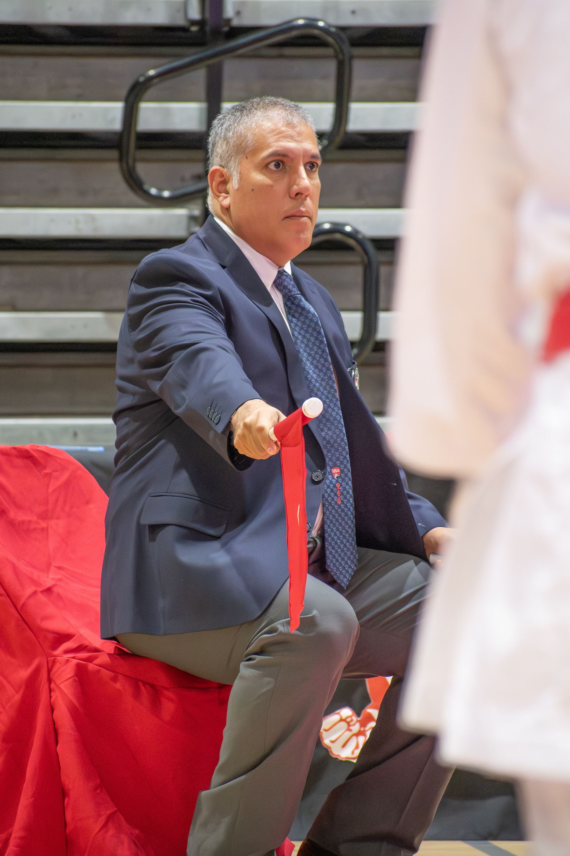 Man in suit holds red ribbon in a gymnasium.