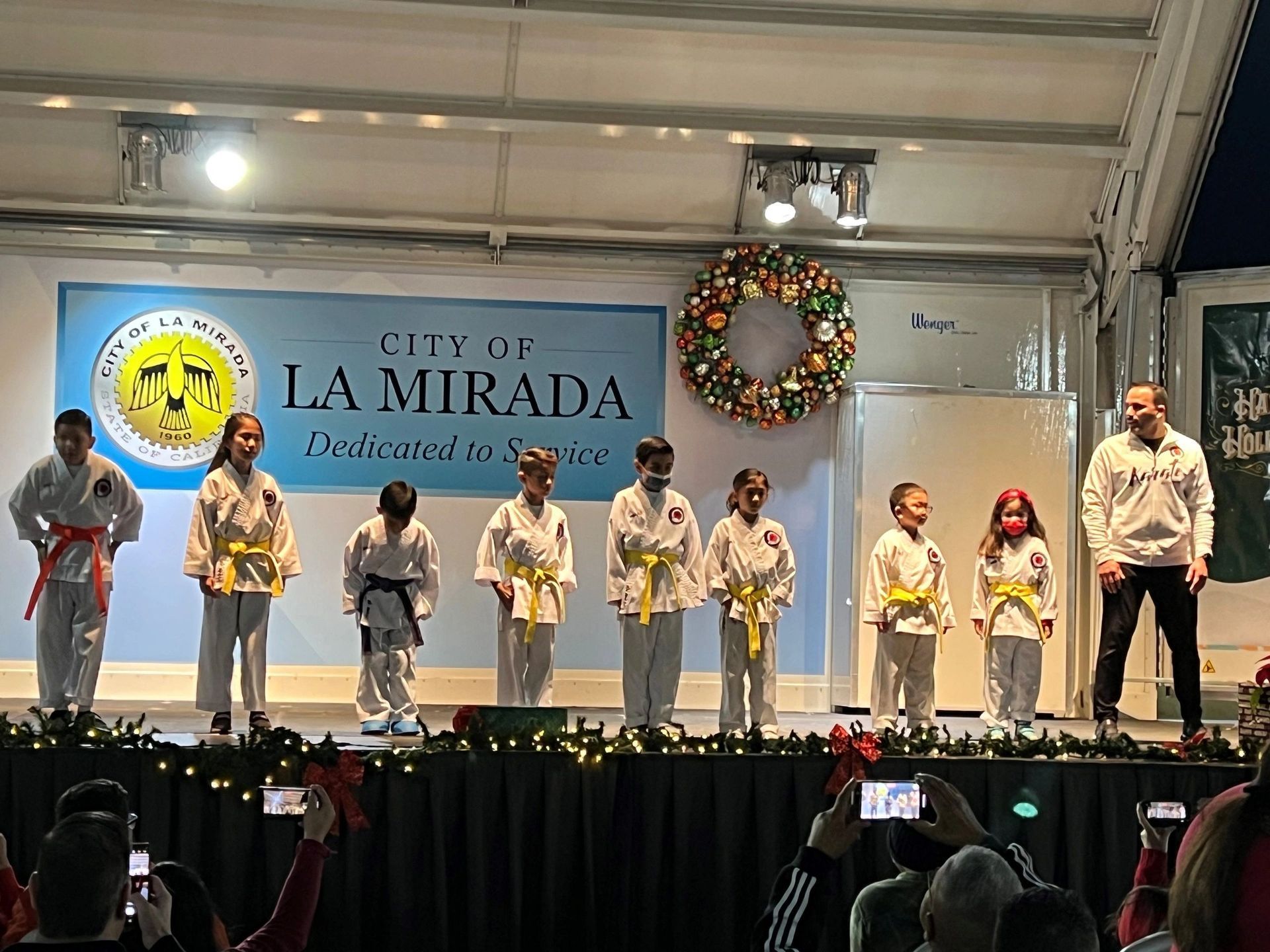 A group of children are standing on a stage in front of a sign that says city of la mirada.