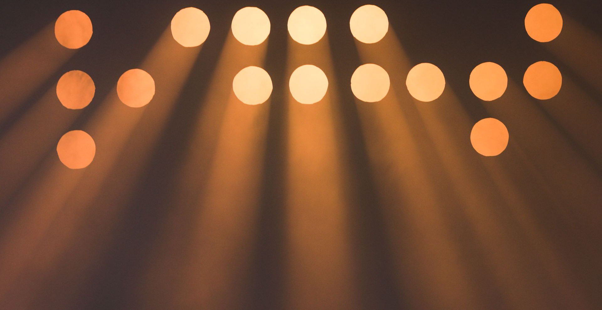 Warm orange stage lights glowing in a dark background, casting beams downward