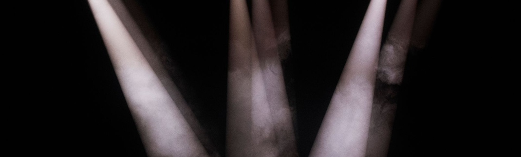 Three pale spotlights shining upward in a dark scene