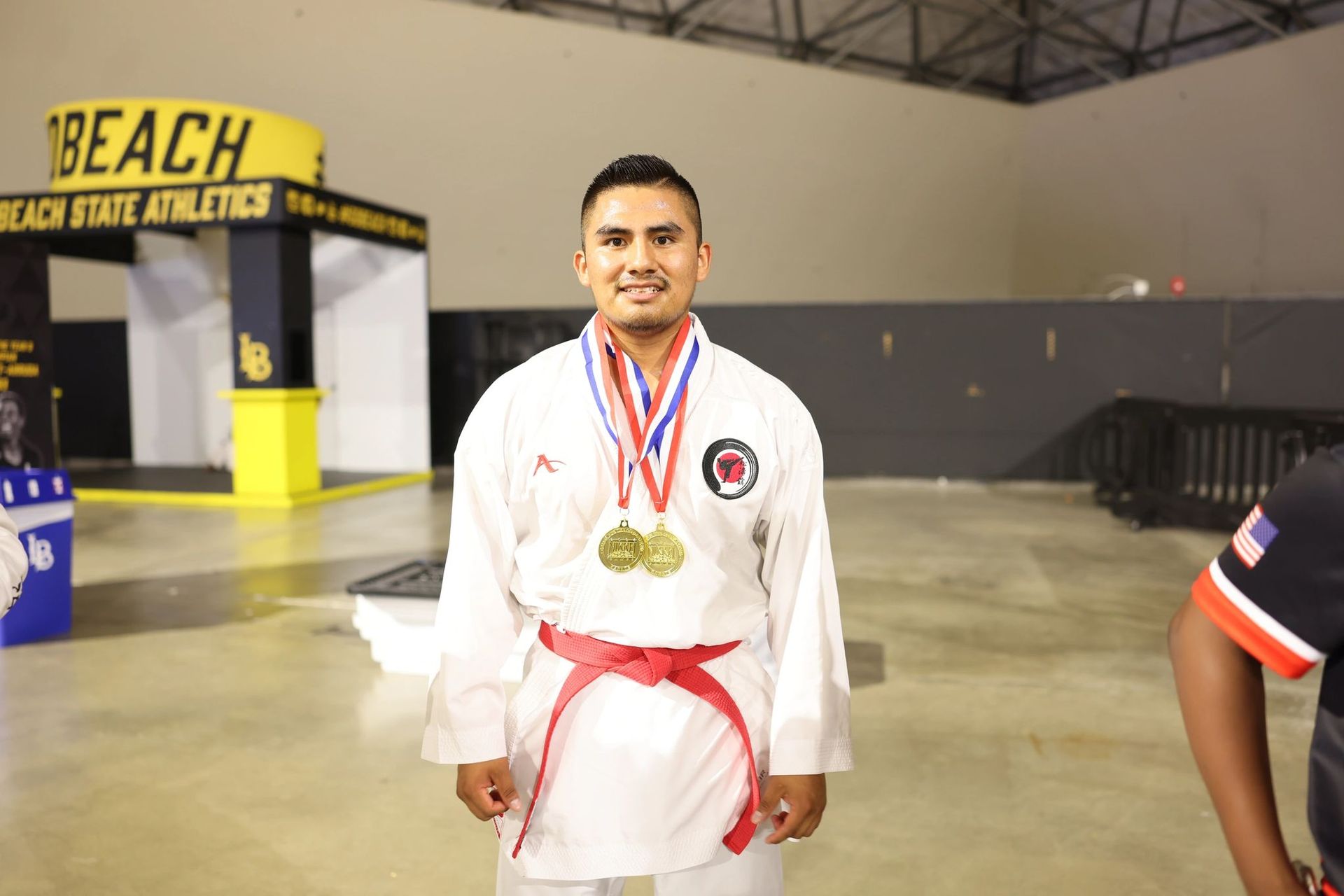 A man in a white karate uniform is standing in front of a beach state athletics booth