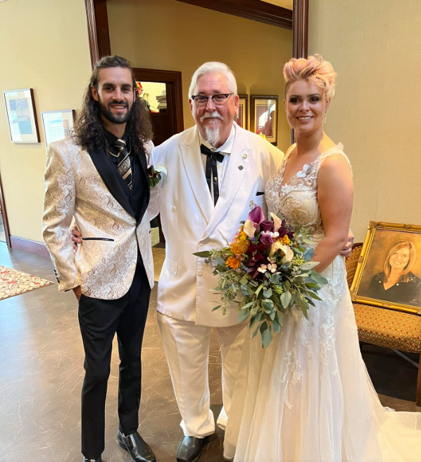 A bride and groom pose for a picture with their father