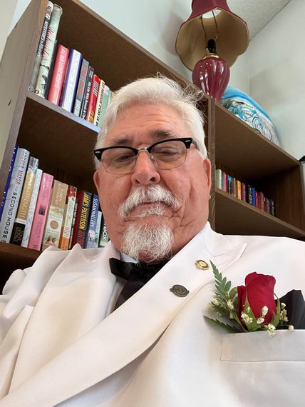 A man in a white suit with a red rose in his pocket